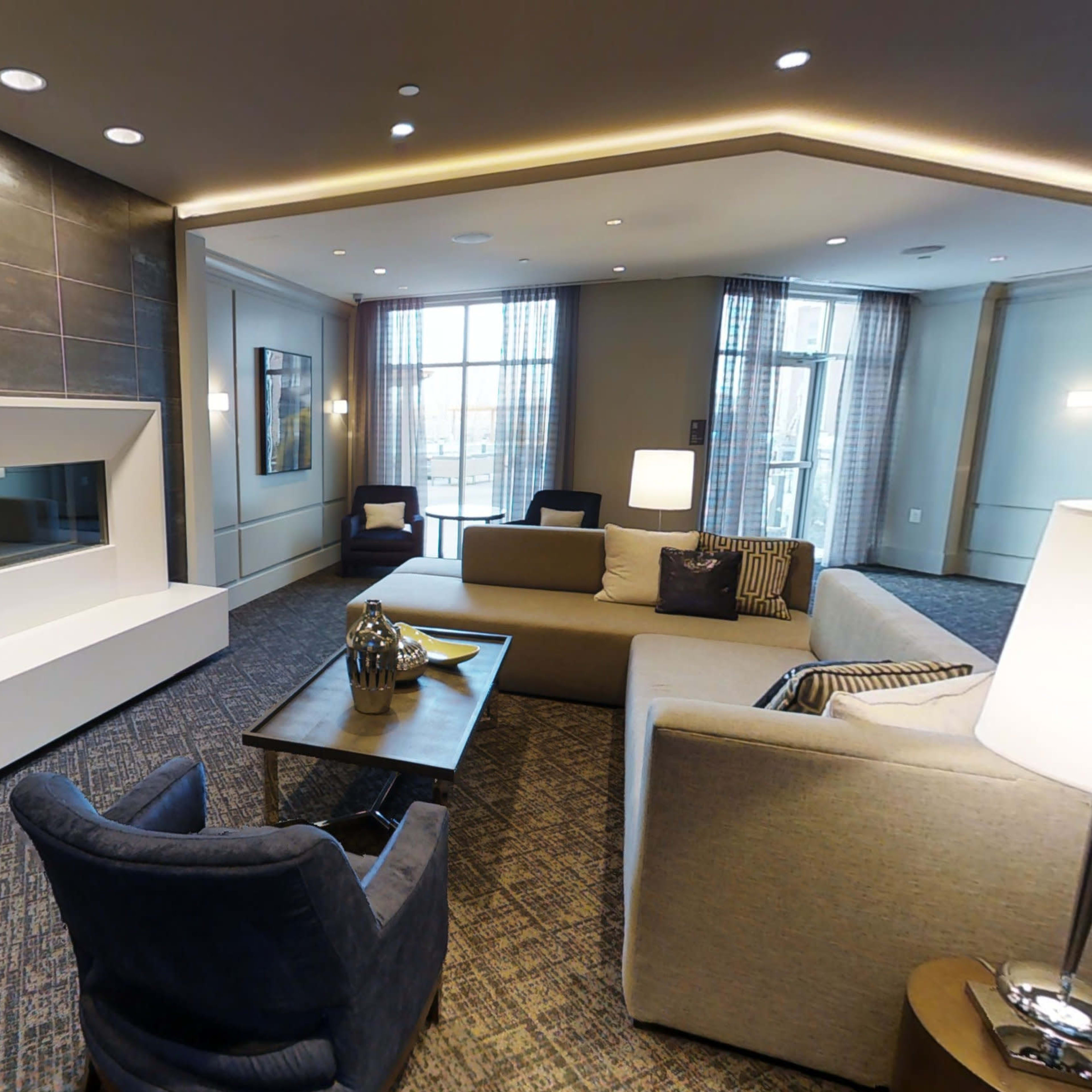 A modern living area features a stylish fireplace, two sofas, a coffee table, and a lamp under soft lighting.