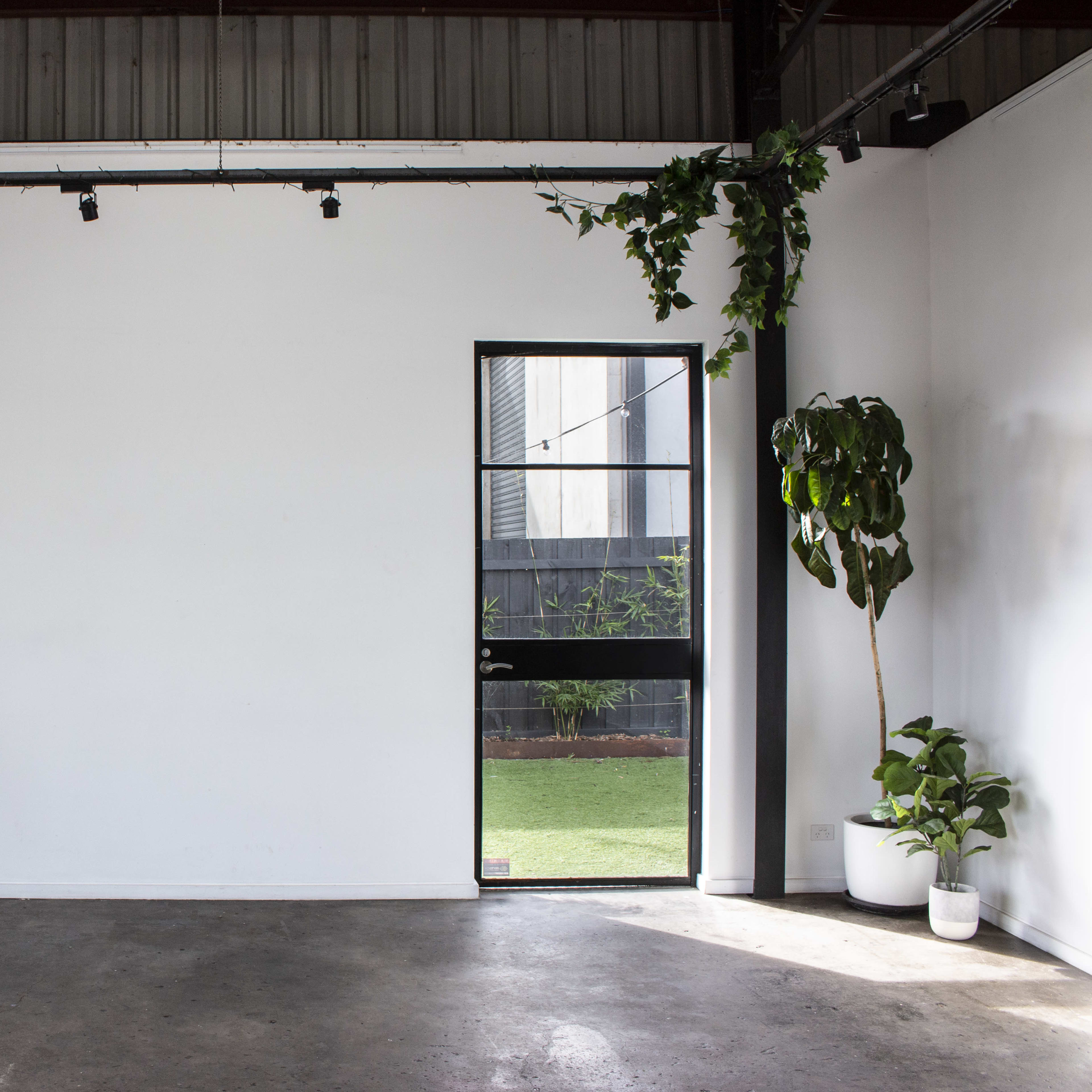 A minimalist interior space with a wooden table on wheels, a potted plant, and a door leading to an outdoor area.