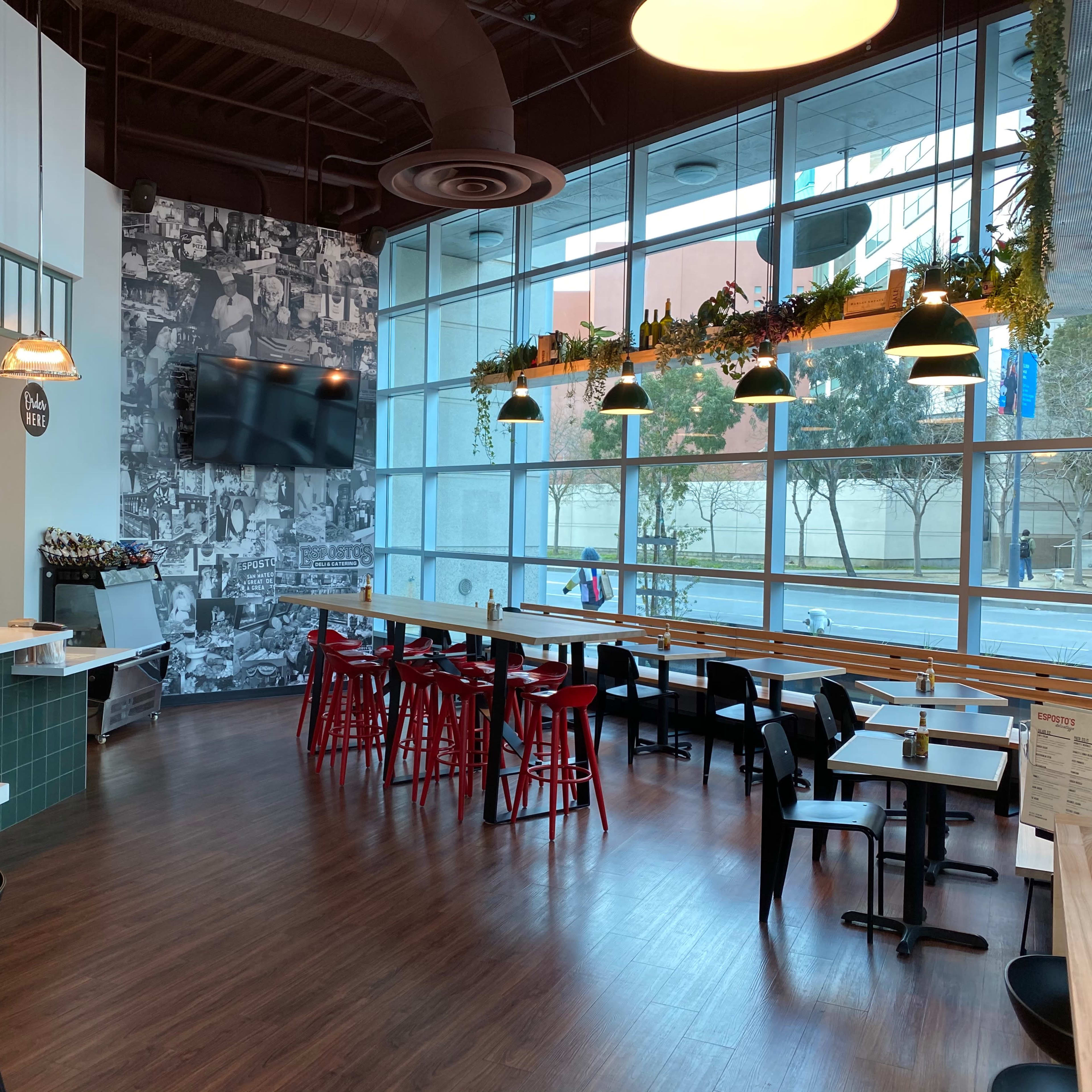 A modern dining area with a mix of black and red chairs, large windows, and a wall covered in black-and-white photos.