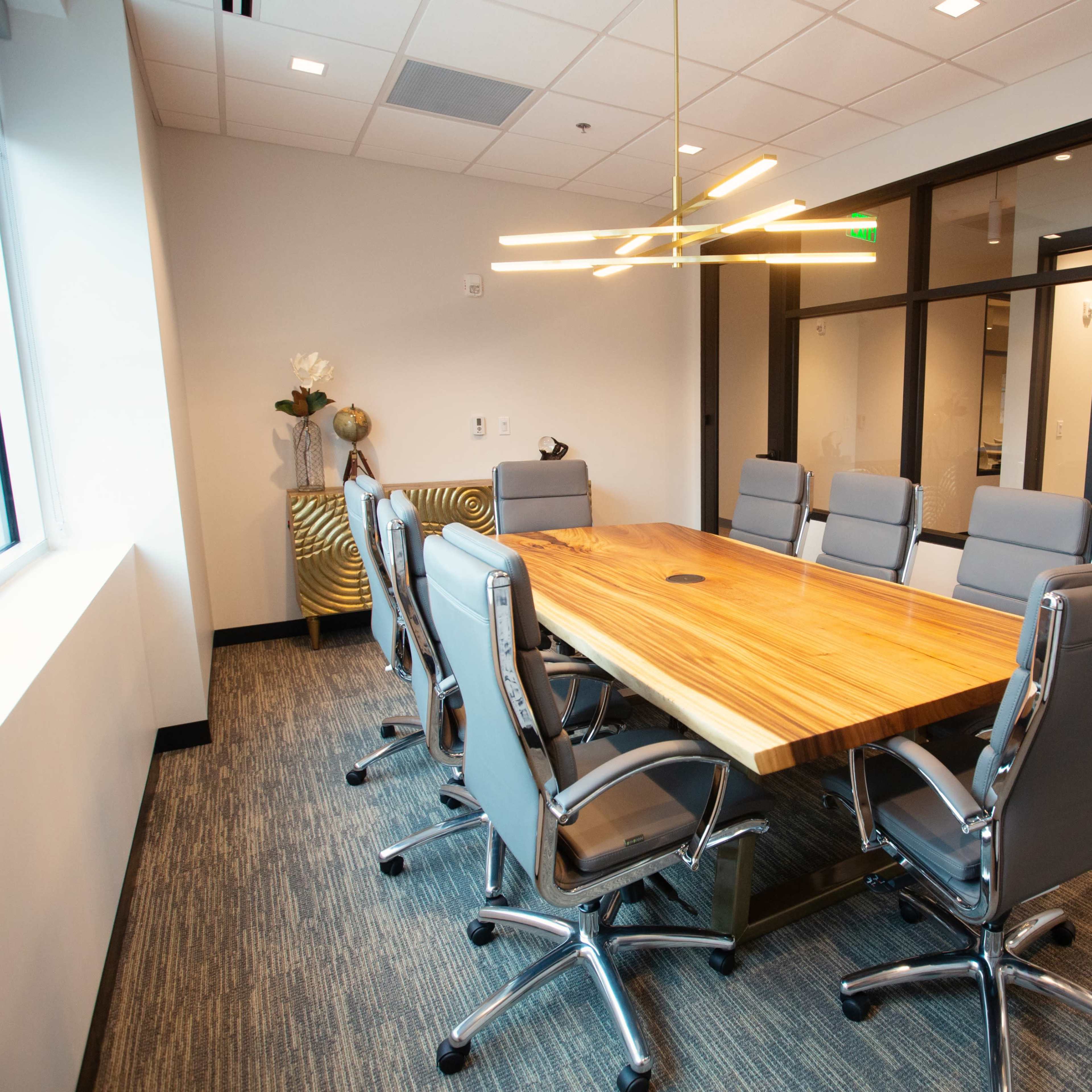 A modern conference room features a large wooden table surrounded by several ergonomic chairs and a stylish light fixture overhead.