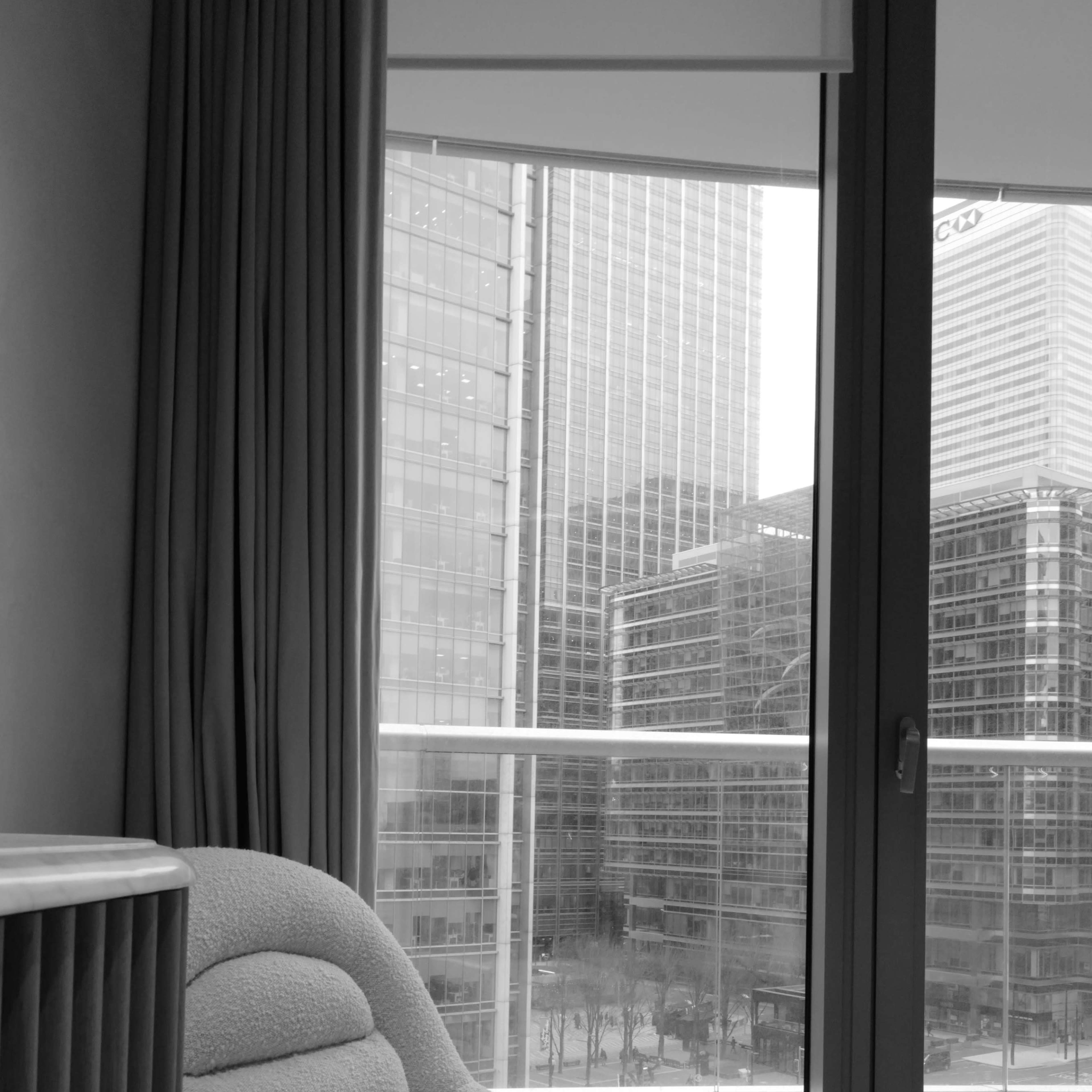 A plush chair sits near a large window, overlooking a cityscape of modern buildings.