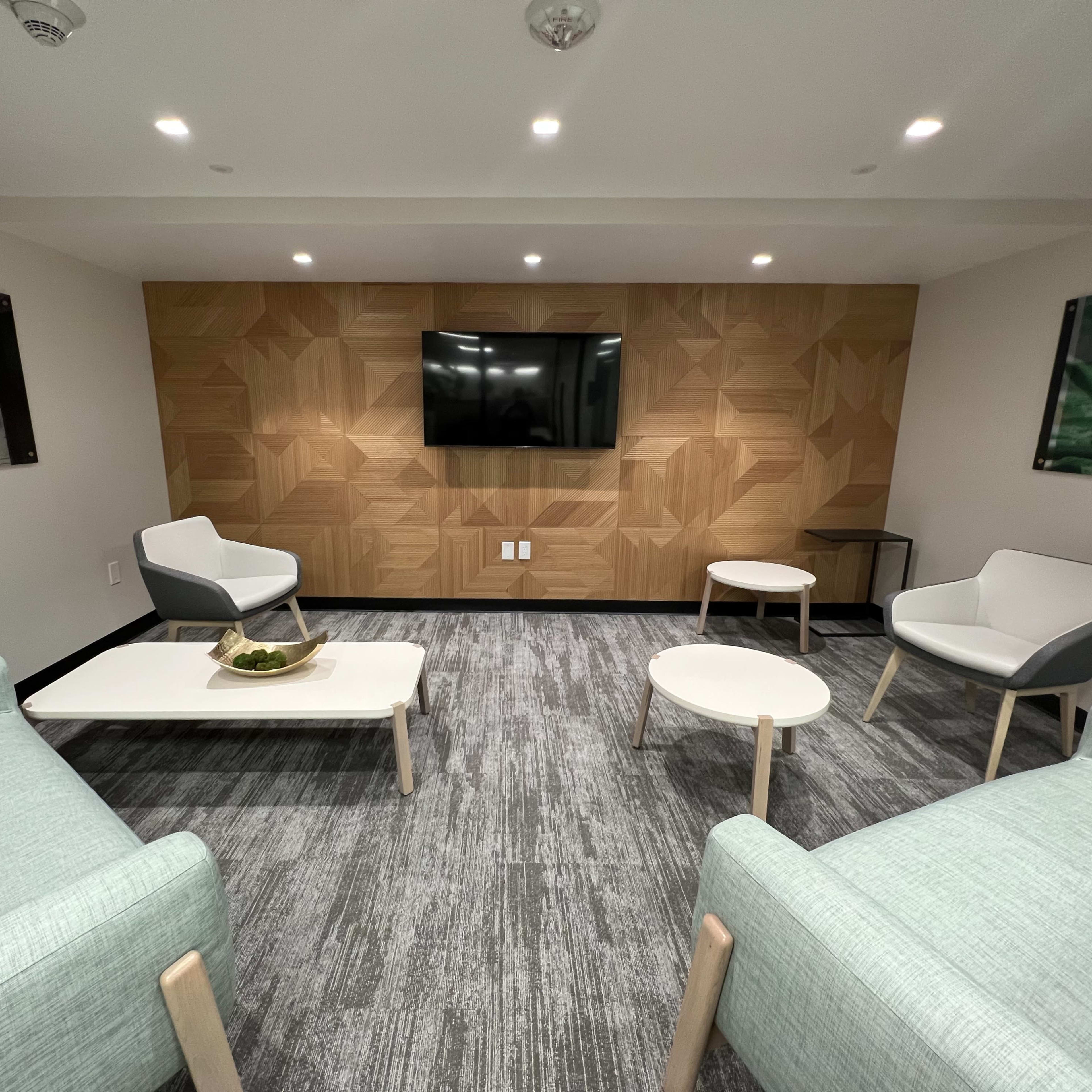 A modern lounge area with light green upholstered chairs, a white coffee table, and a wooden feature wall with a TV.