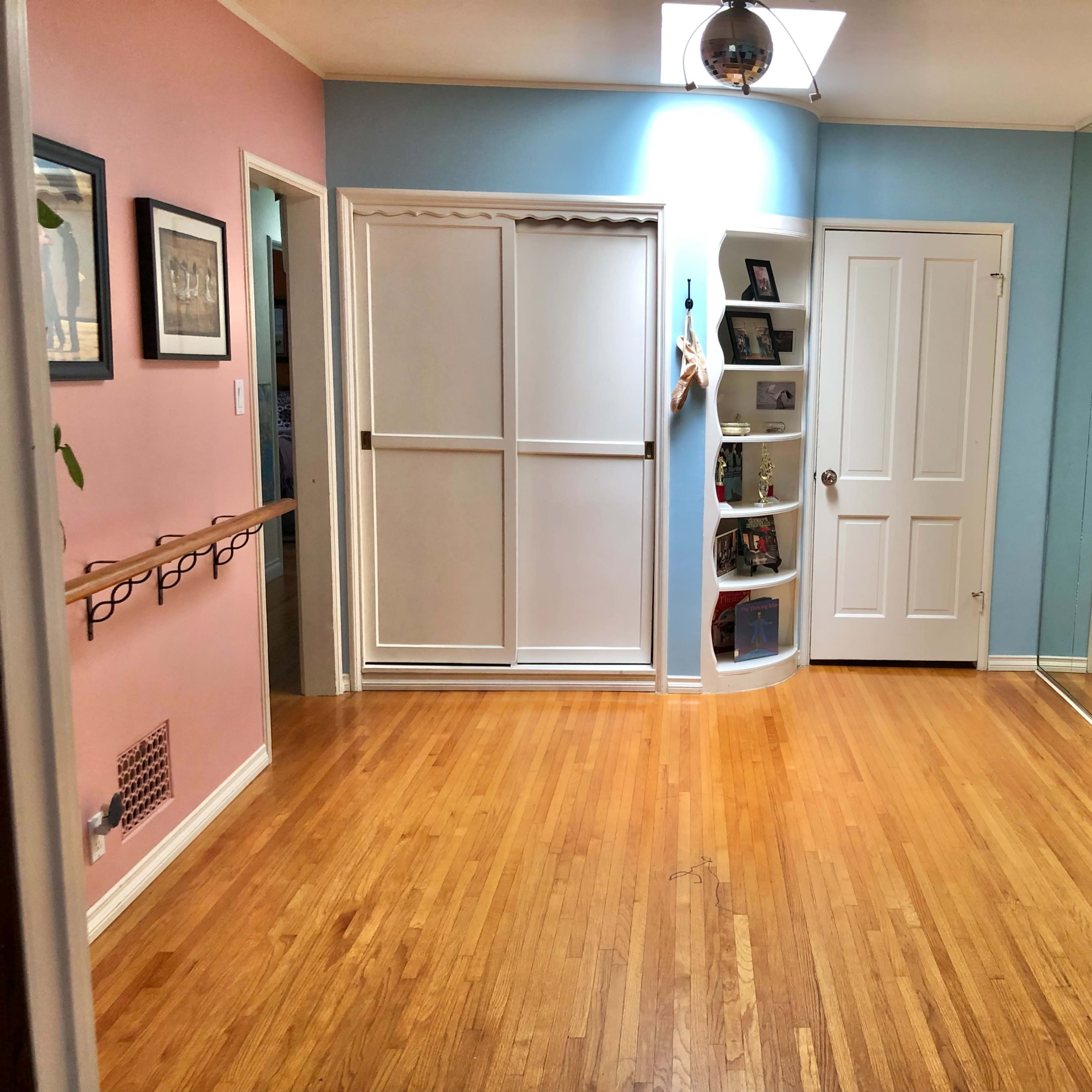 A room with hardwood floors, pale pink and blue walls, and mirrored closet doors.