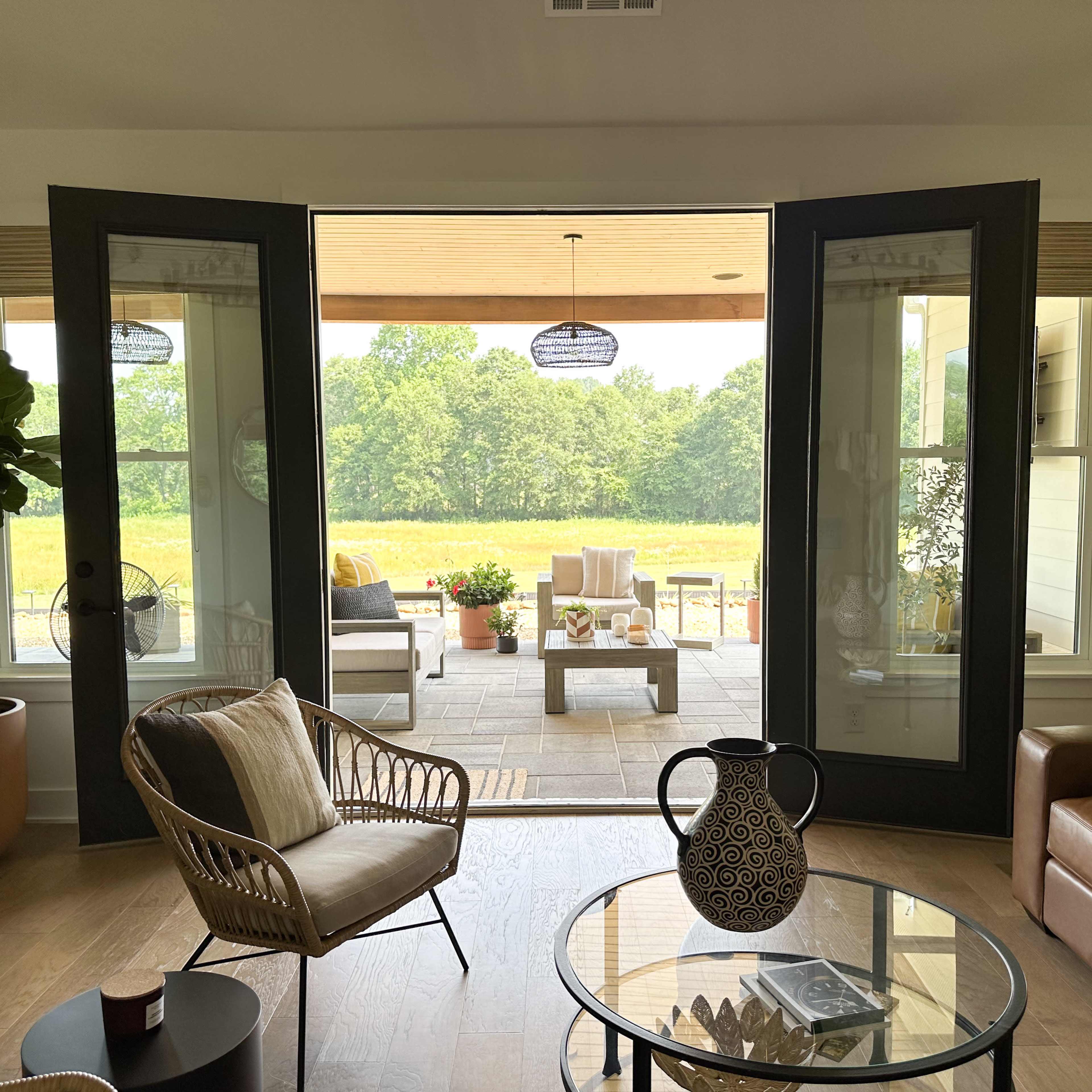 A living room with open double doors leading to a patio area surrounded by greenery.