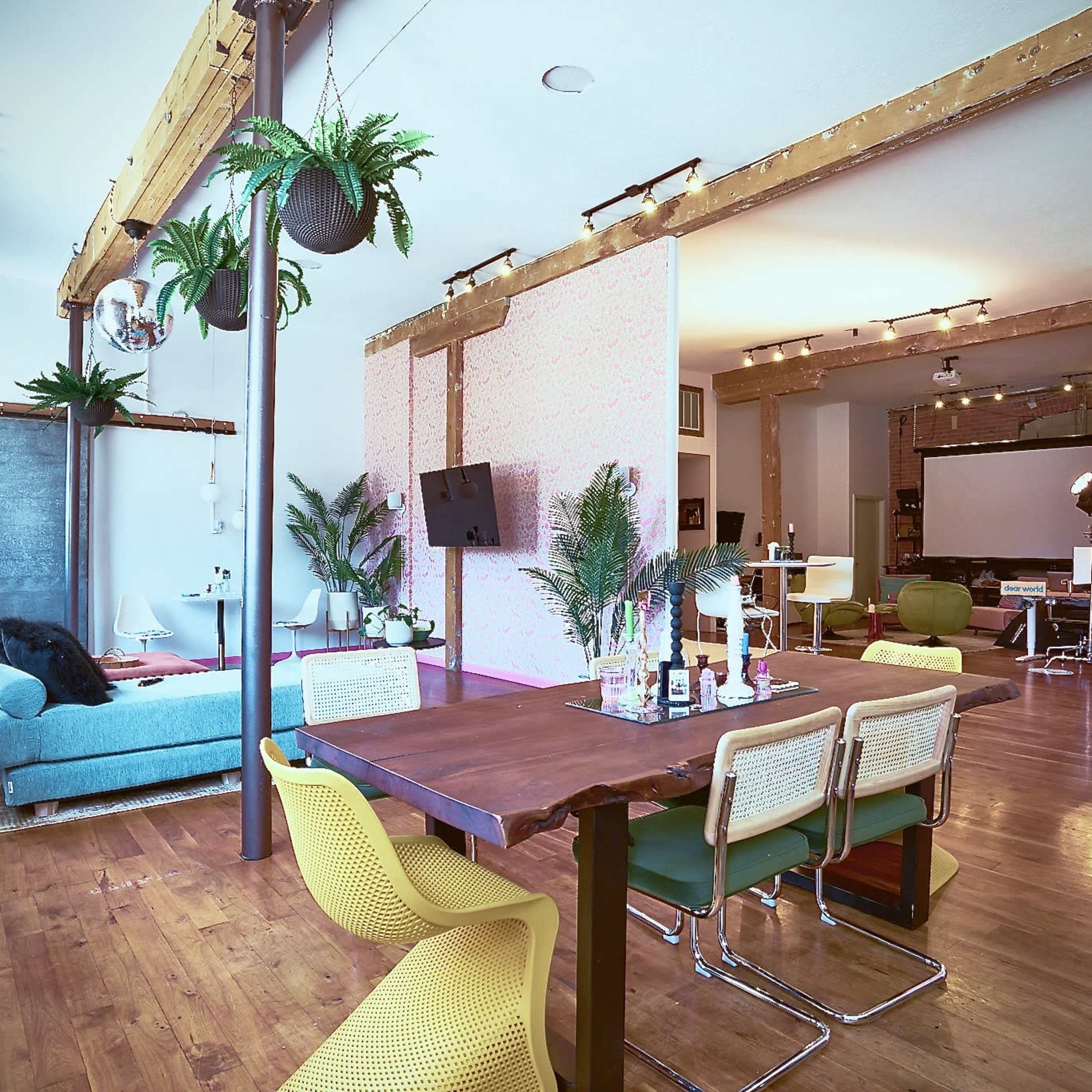 A spacious and modern open-concept living area with a dining table, a cozy seating area, and large windows, adorned with indoor plants and various furnishings.