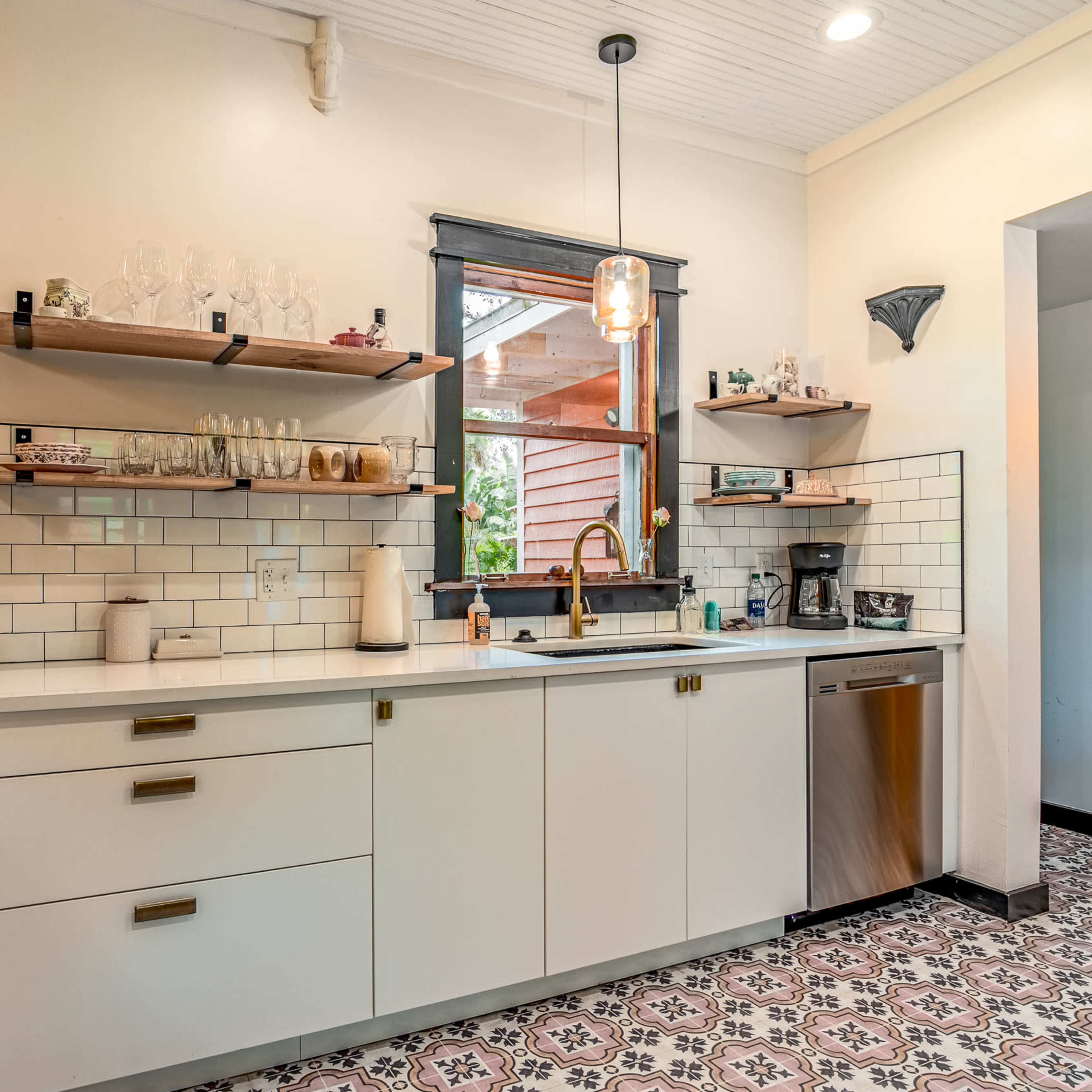 A modern kitchen features white cabinetry, open shelves displaying glassware, and patterned tile flooring.
