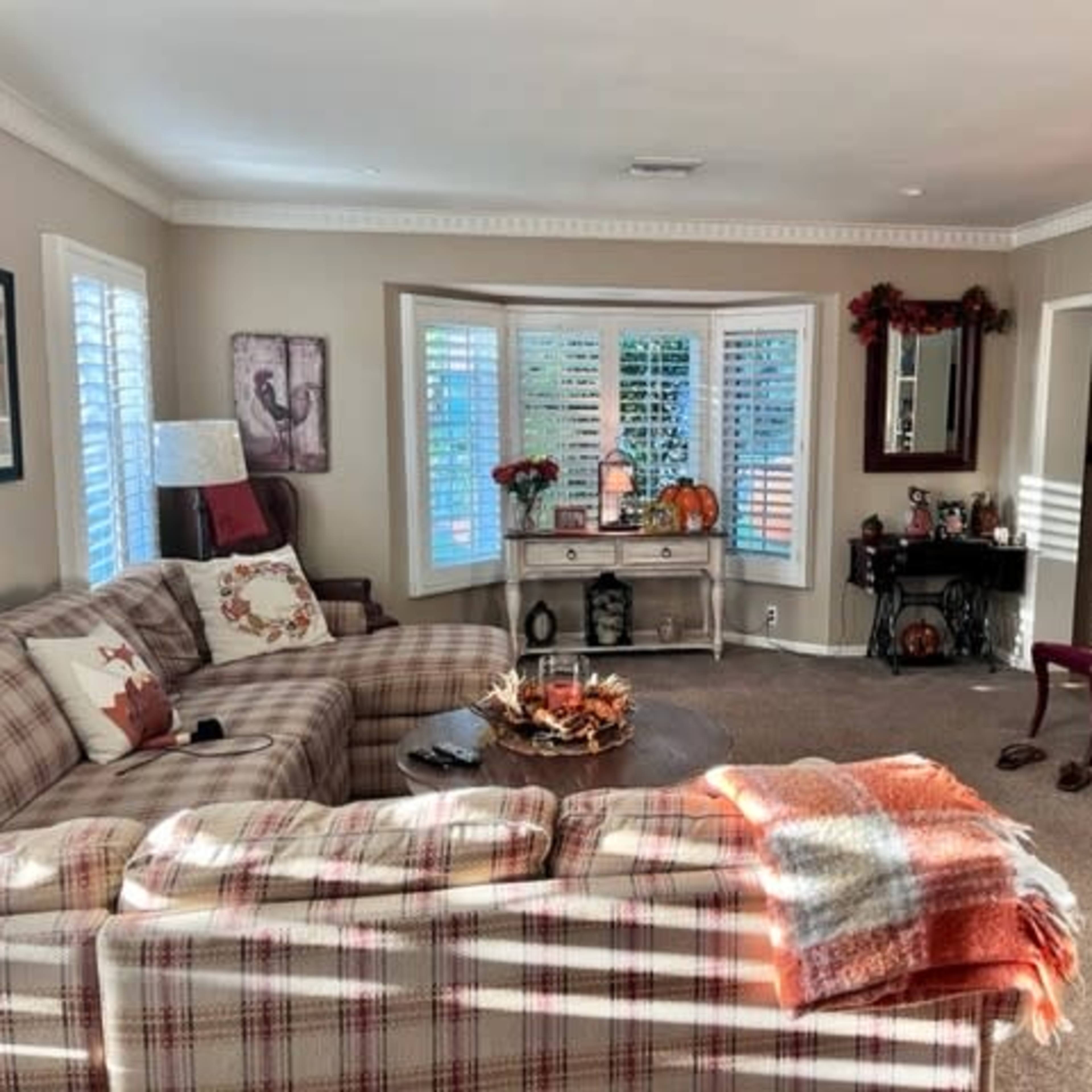 A cozy living room featuring a plaid sectional sofa, a decorative coffee table, and a fireplace surrounded by seasonal decorations.