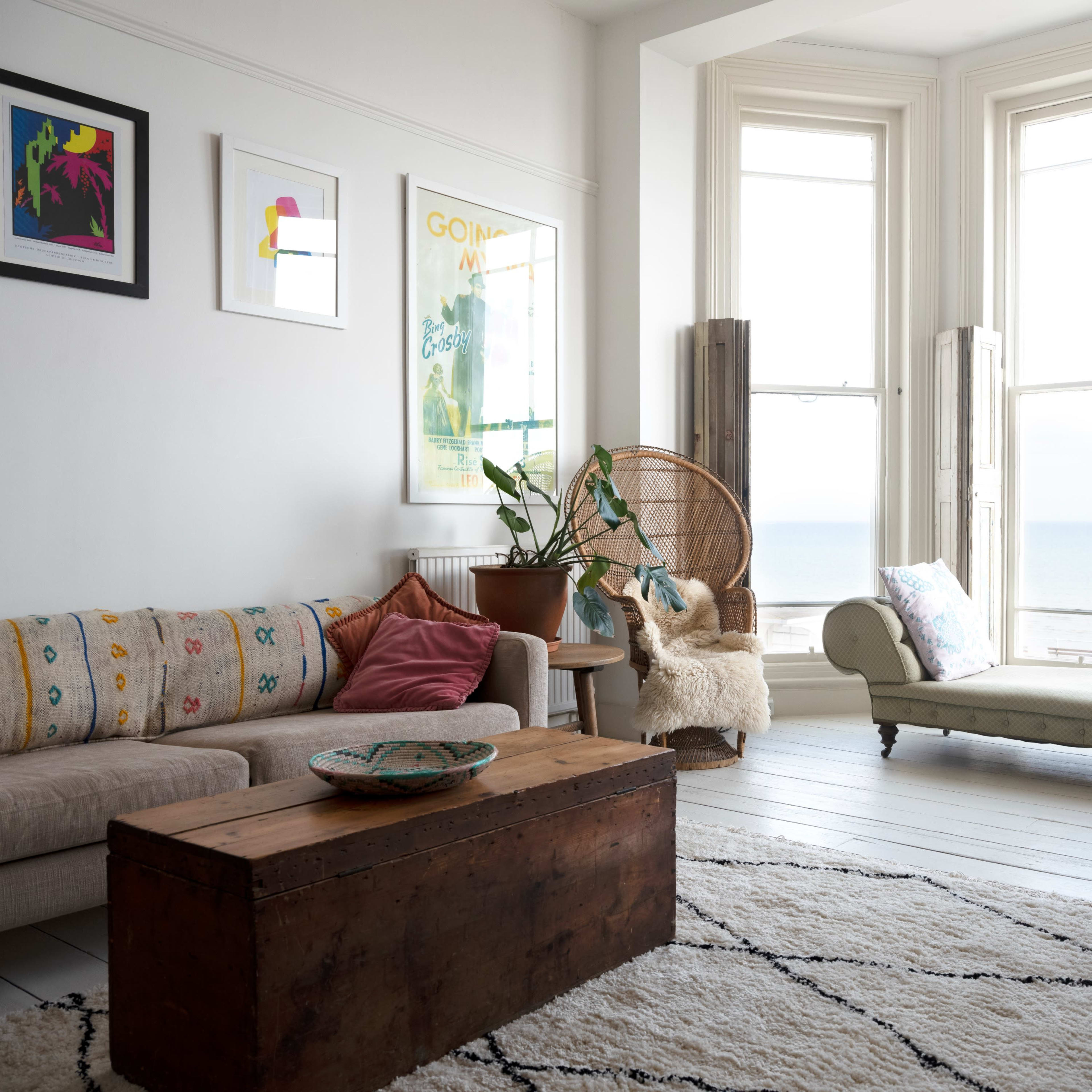 A bright living room with a sofa, a wooden coffee table, a vintage chaise lounge, and large windows offering a view of the sea.