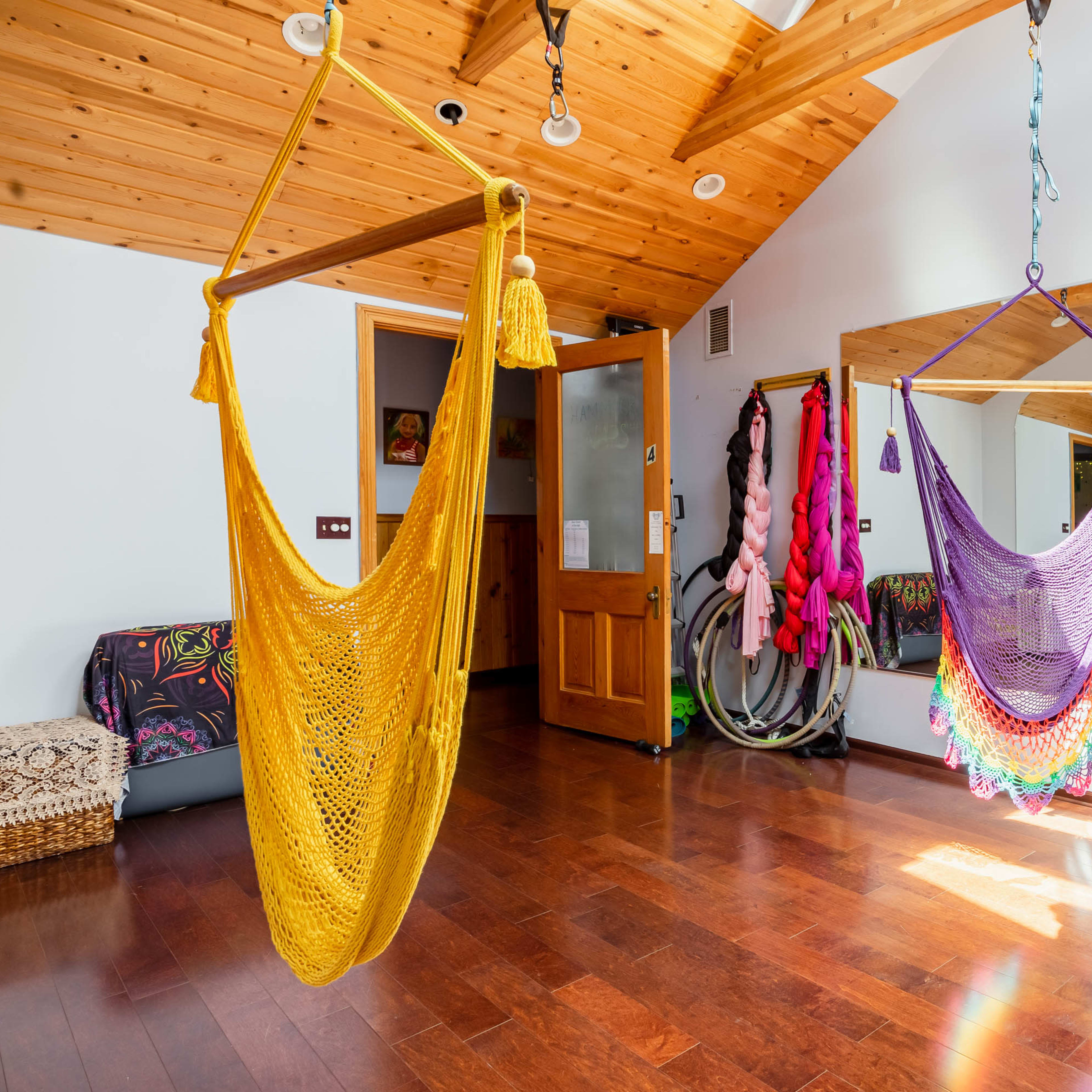 The room features colorful hanging hammocks, wooden ceilings, and a mirror reflecting vibrant wall decorations.