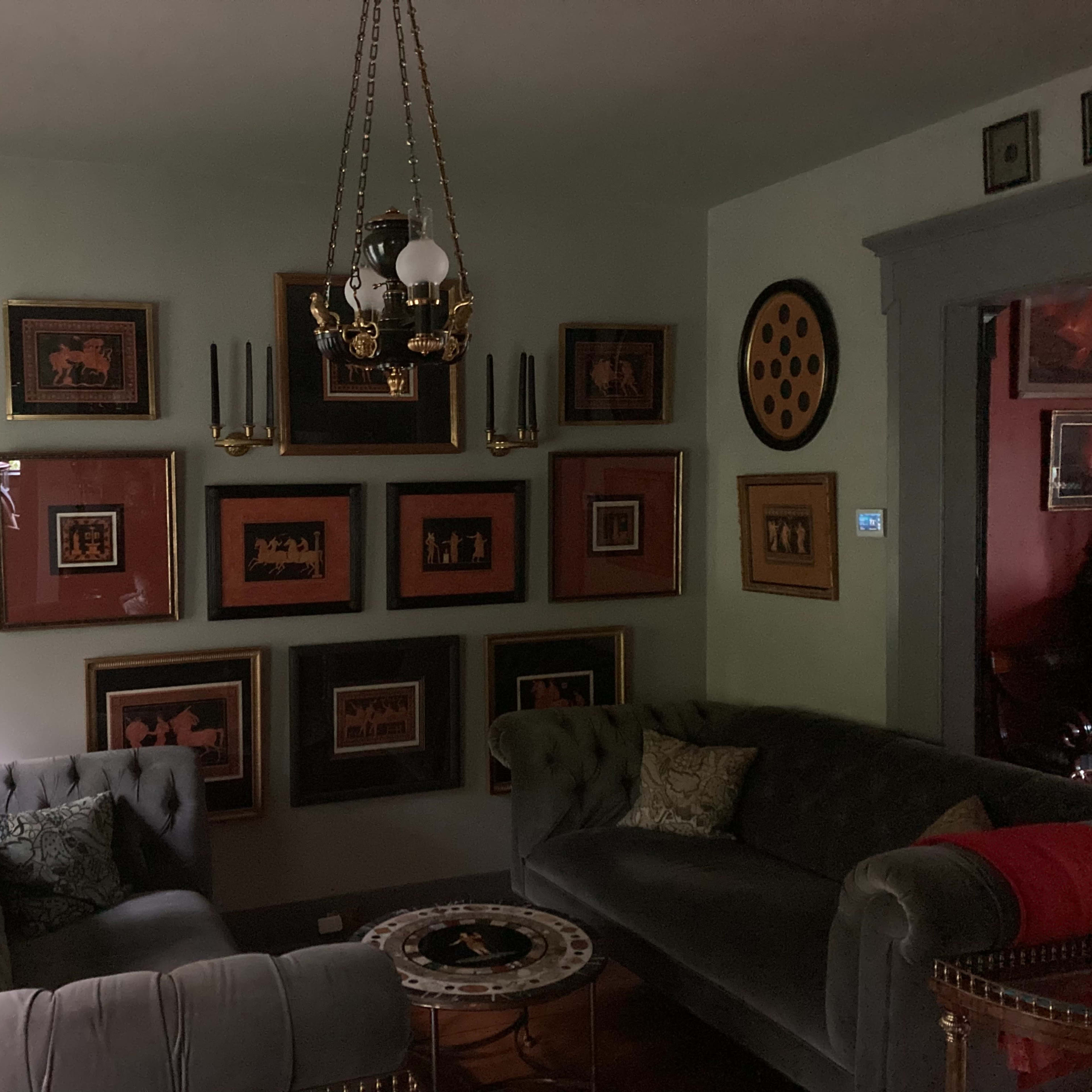 A dimly lit living room with two sofas, a central coffee table, and a wall adorned with framed artwork and decorative items.