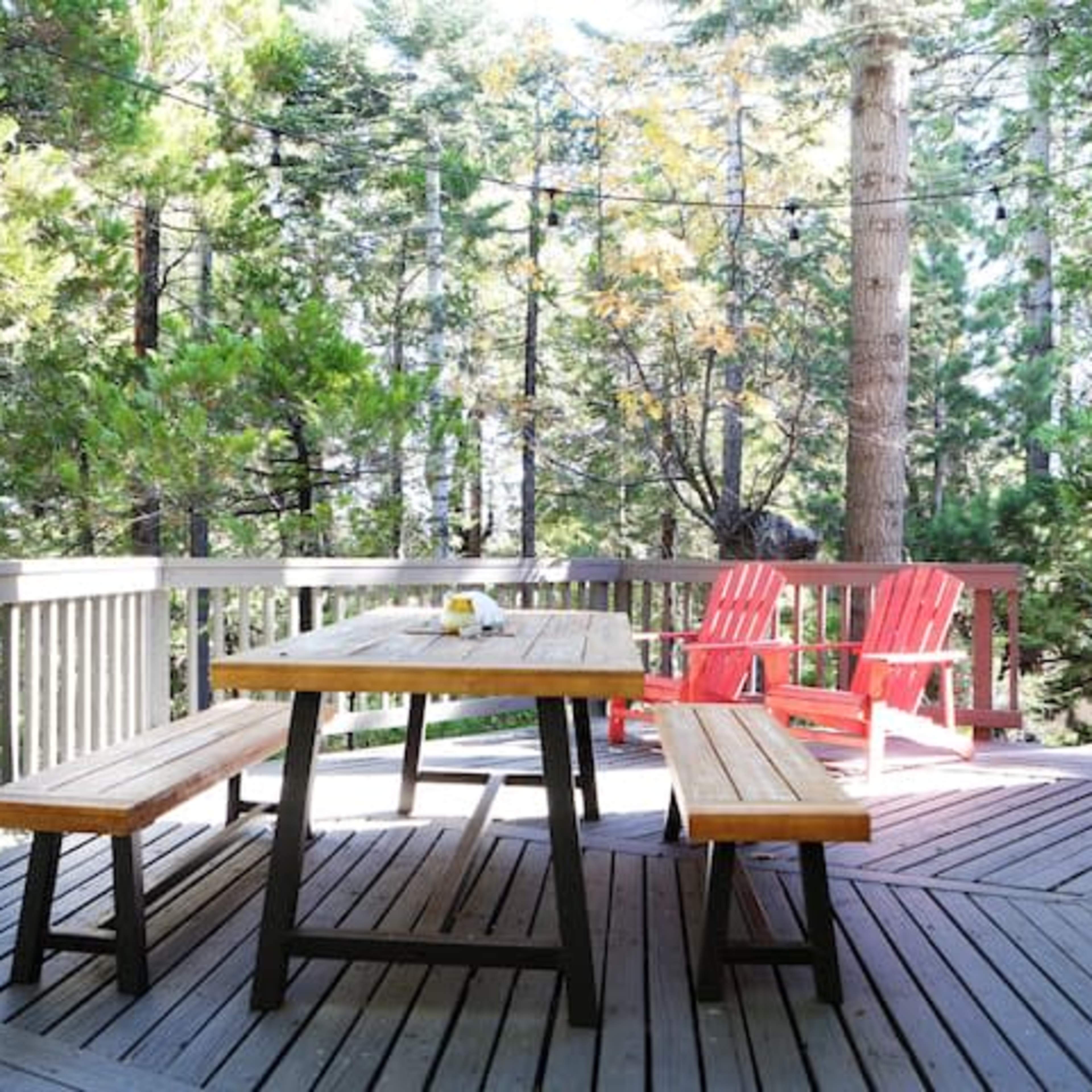 A wooden picnic table with benches is set on a deck surrounded by tall trees.