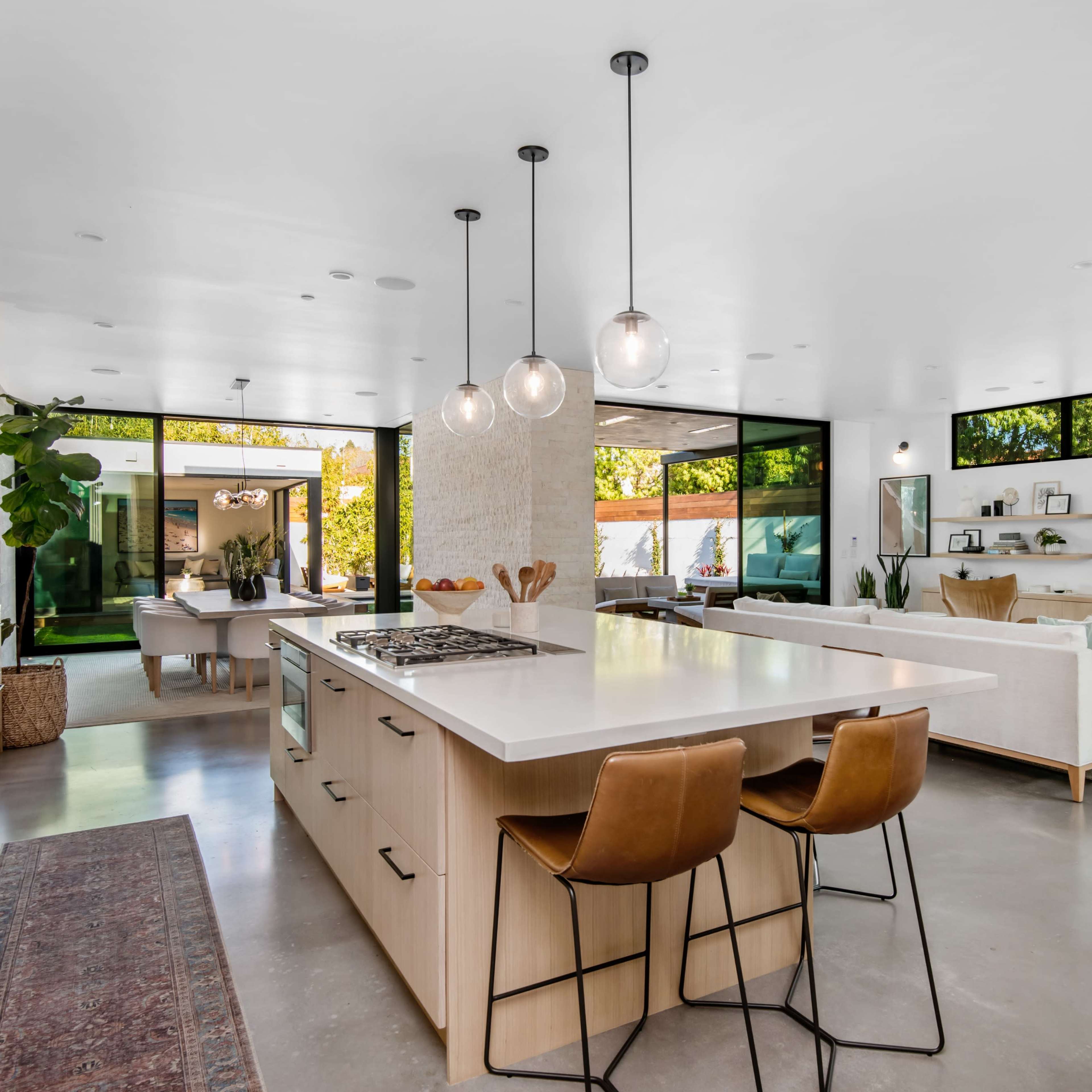 A modern open-concept kitchen and living area with large windows, a central island with seating, and contemporary furnishings.