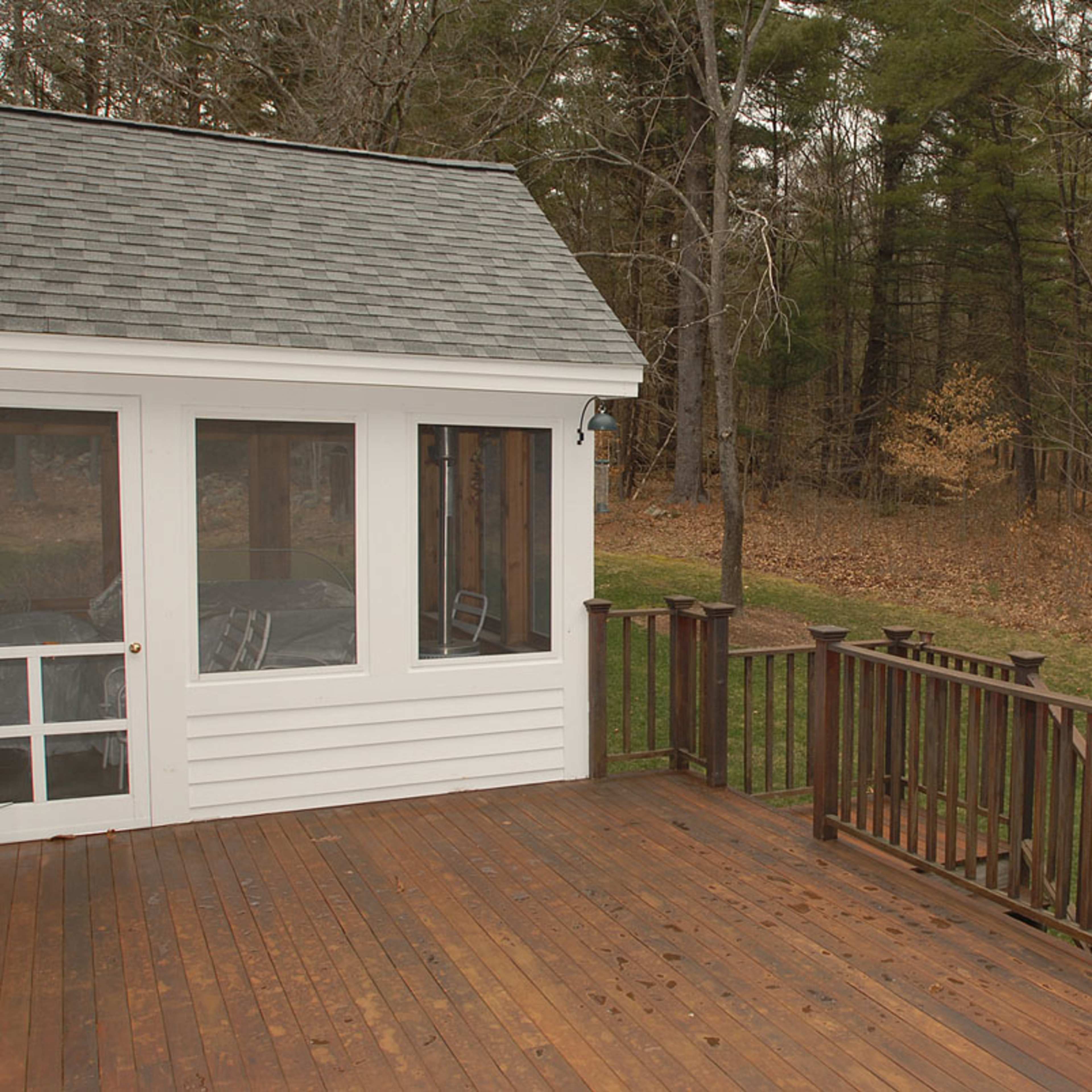 A wooden deck attached to a small white building, overlooking a tree-lined area with sparse foliage.