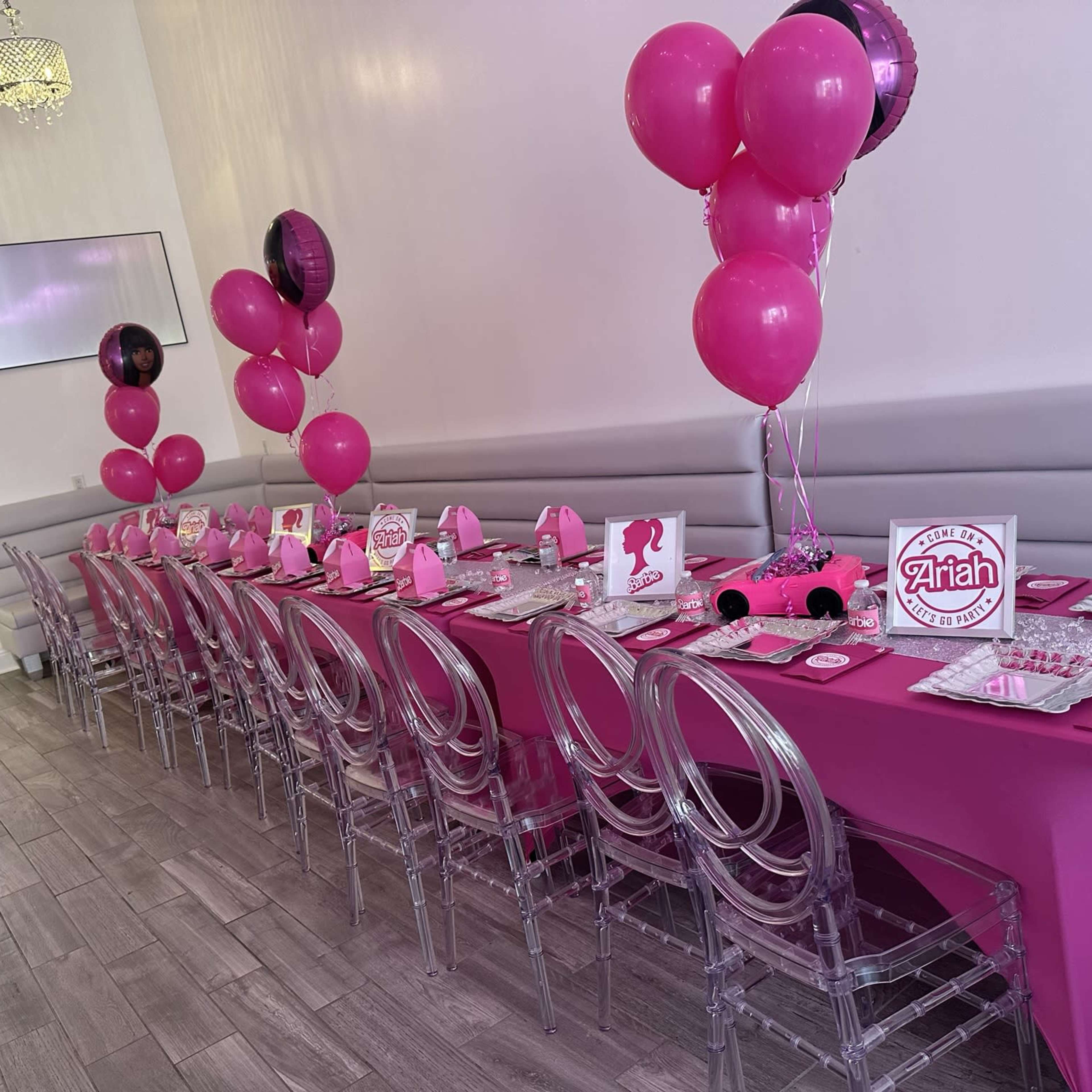 A long, elegantly set party table is adorned with pink decorations, balloons, and themed party supplies.