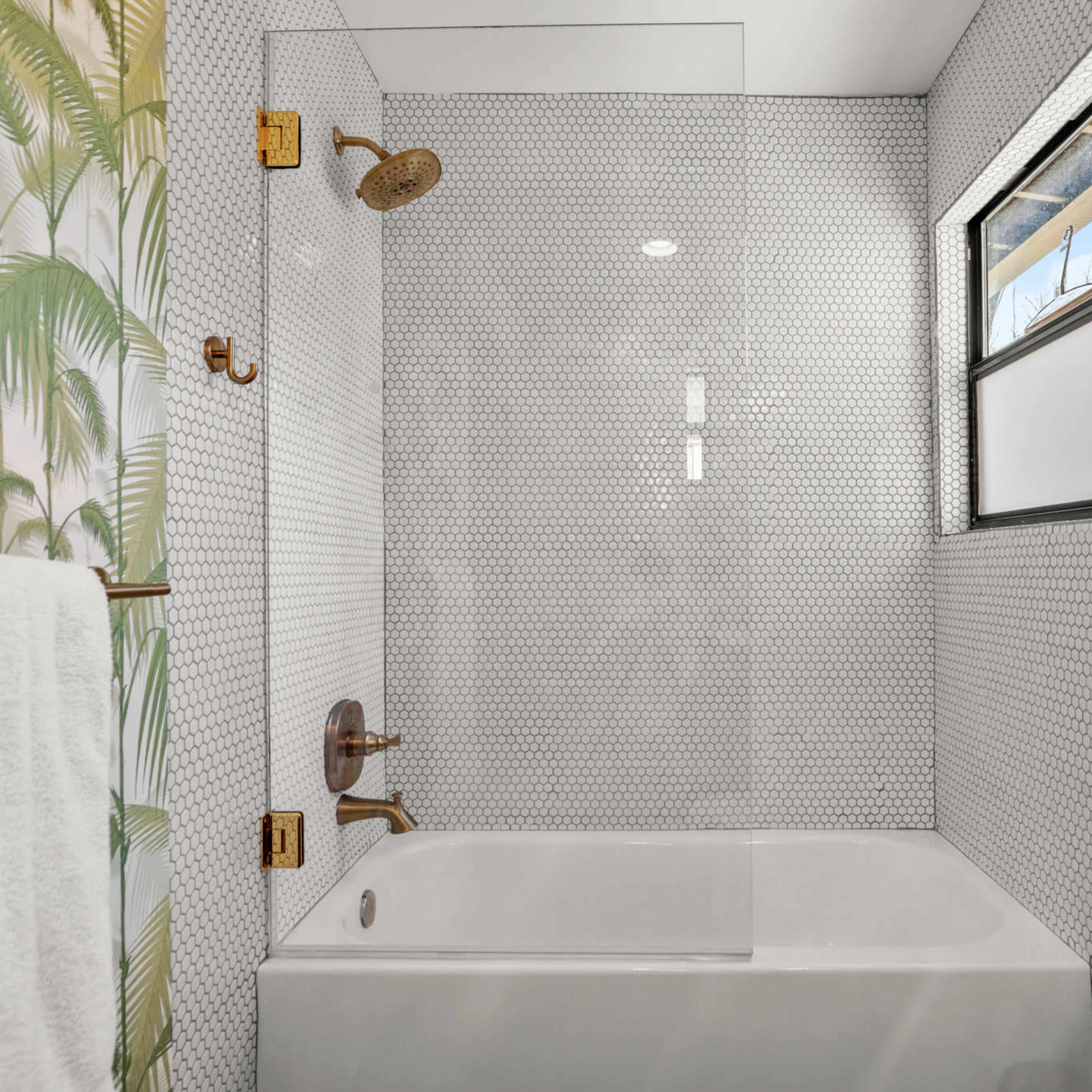 A modern bathroom featuring a white bathtub surrounded by tile and tropical palm leaf wallpaper.