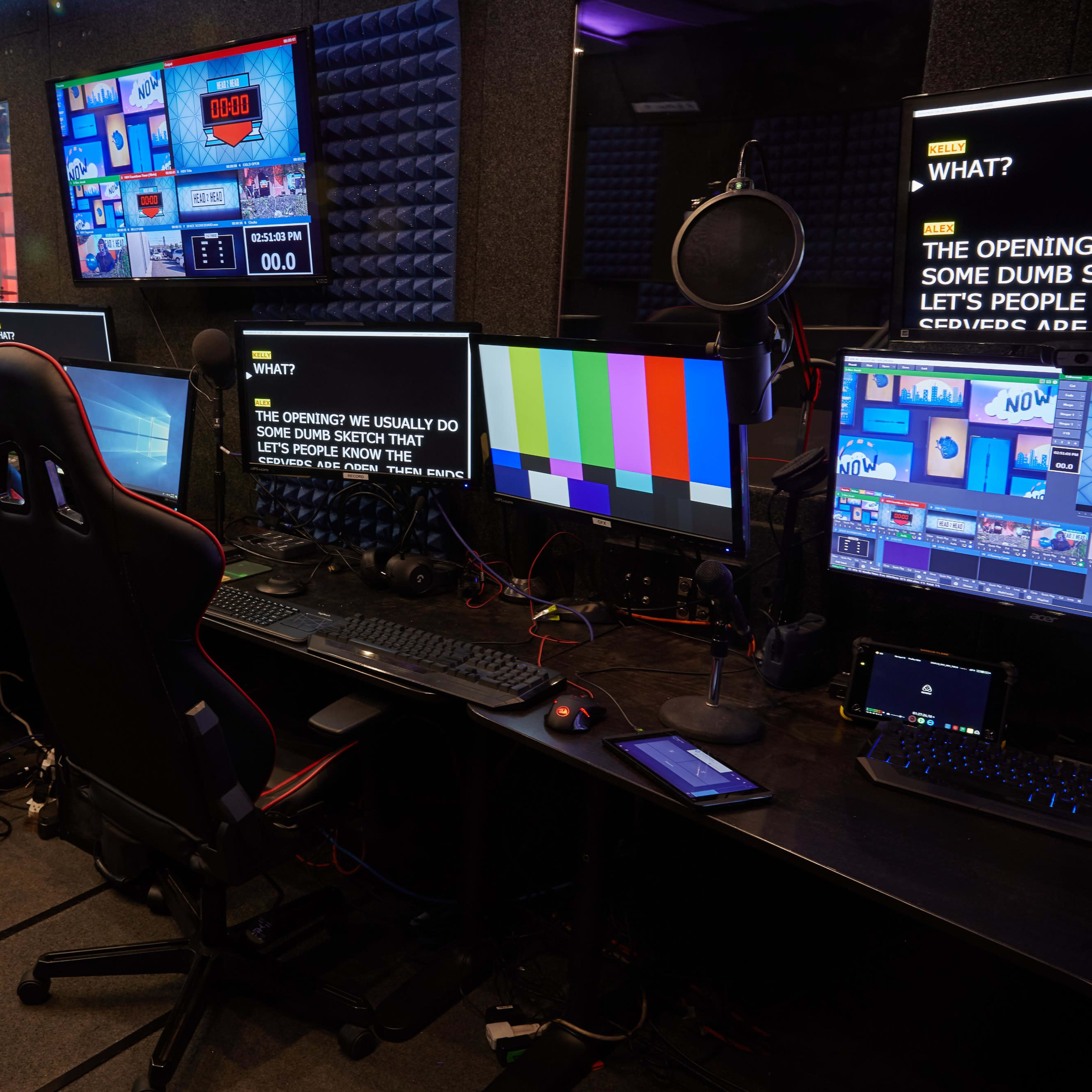 A modern video production control room with multiple monitors, camera equipment, and three office chairs.