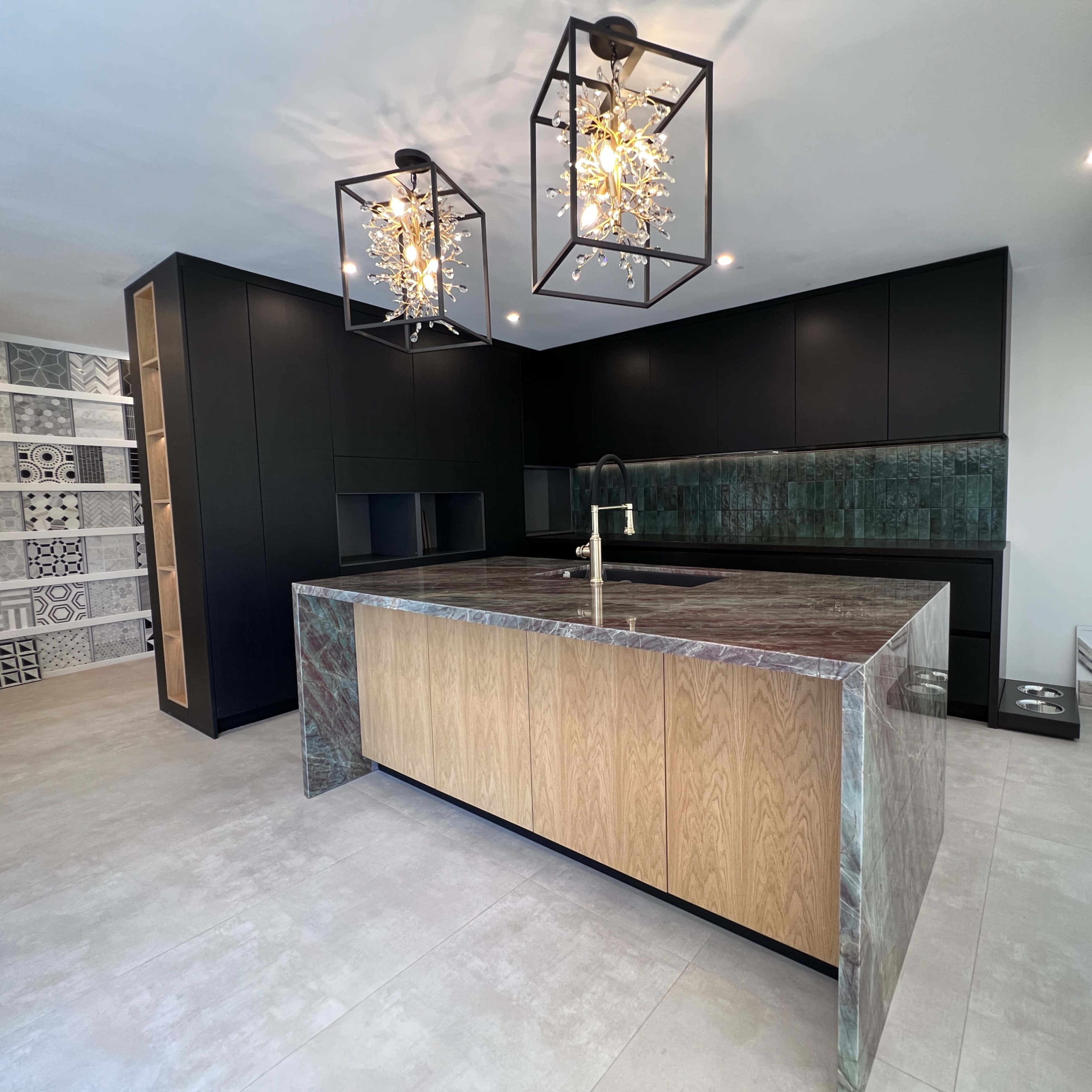 A modern kitchen featuring an island with an oak front and a green stone countertop, black cabinets, and decorative light fixtures.