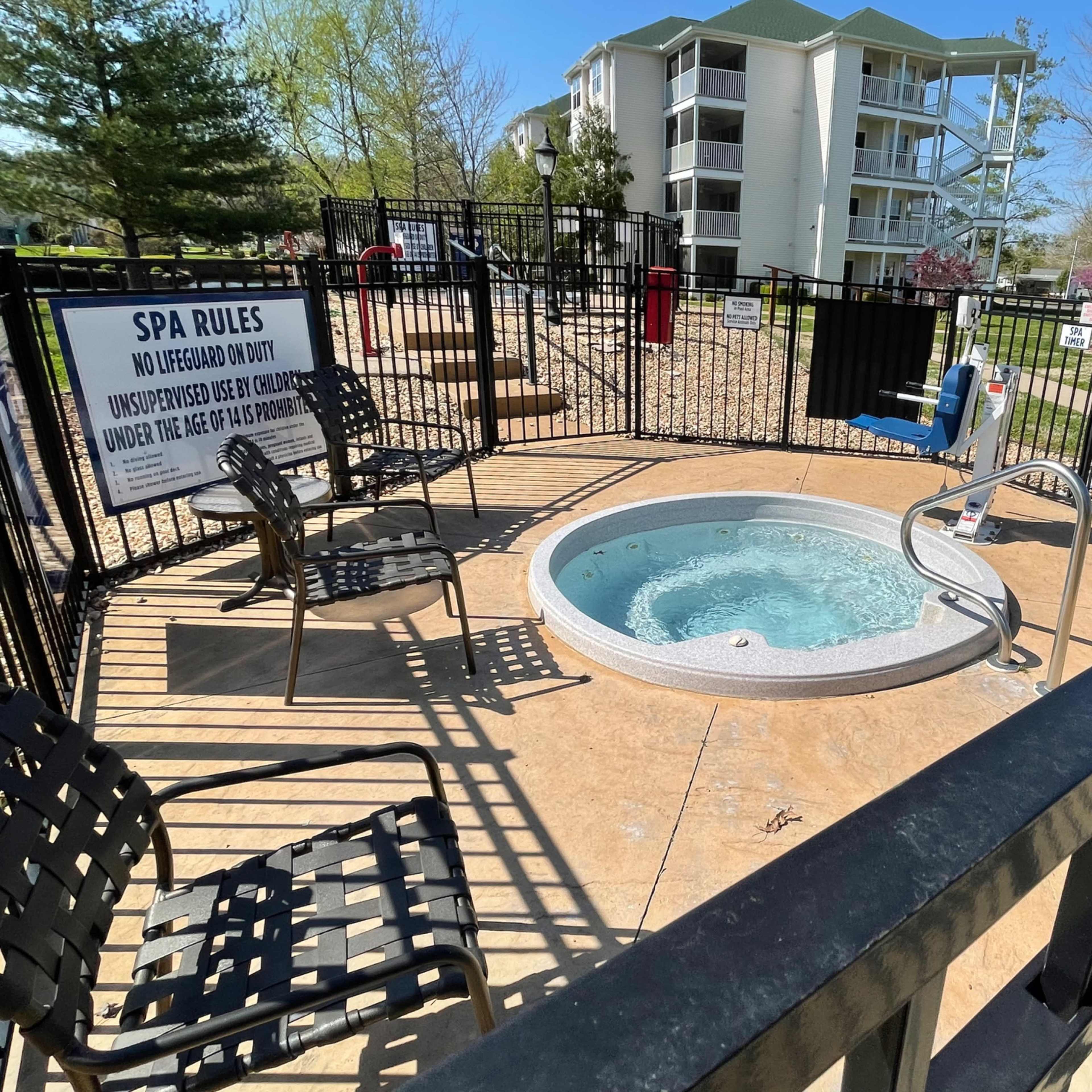 A hot tub is enclosed by a fence with seating and a sign displaying spa rules in a residential area.