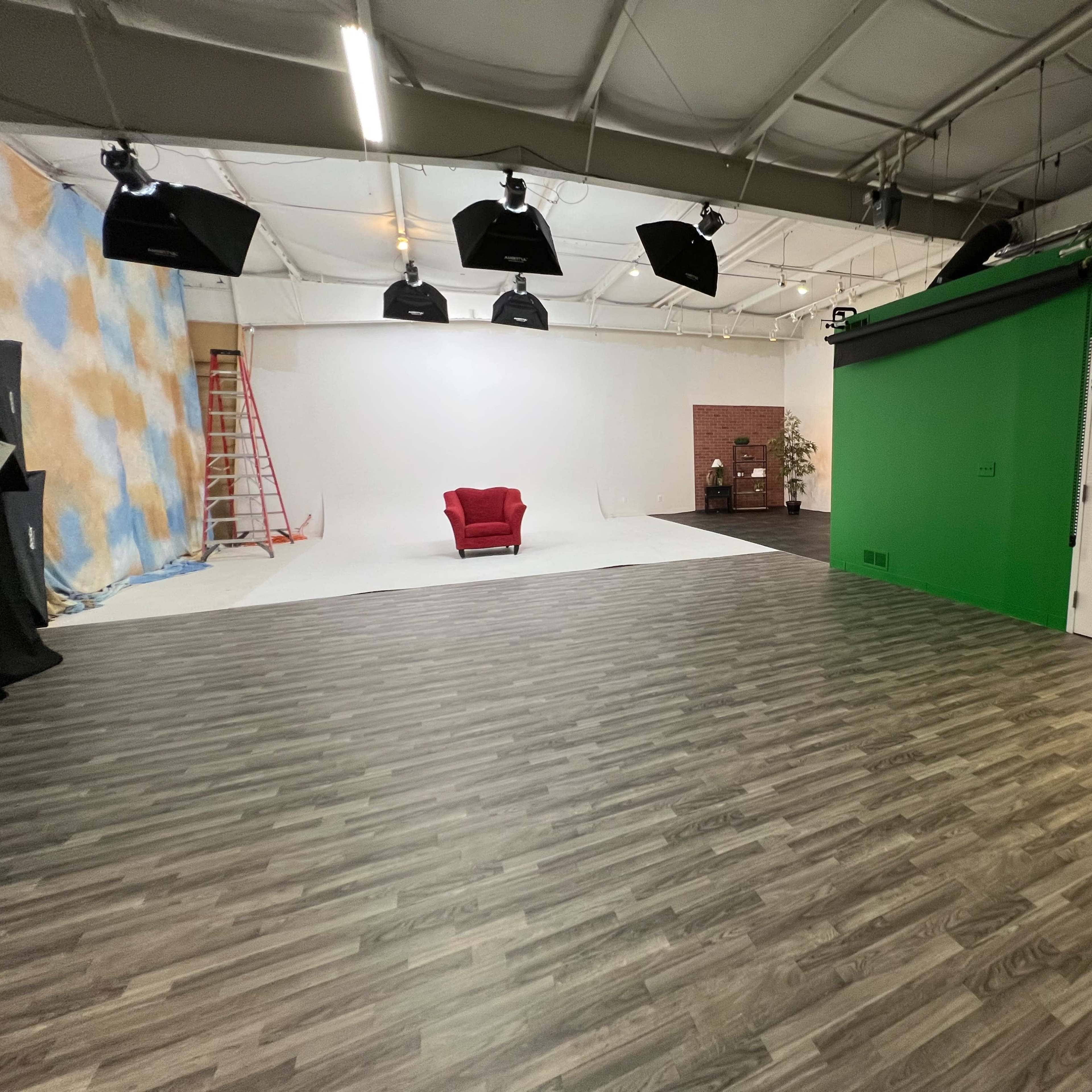 A photography studio with a red chair positioned on a white backdrop, surrounded by green and blue panels and a ladder in the background.