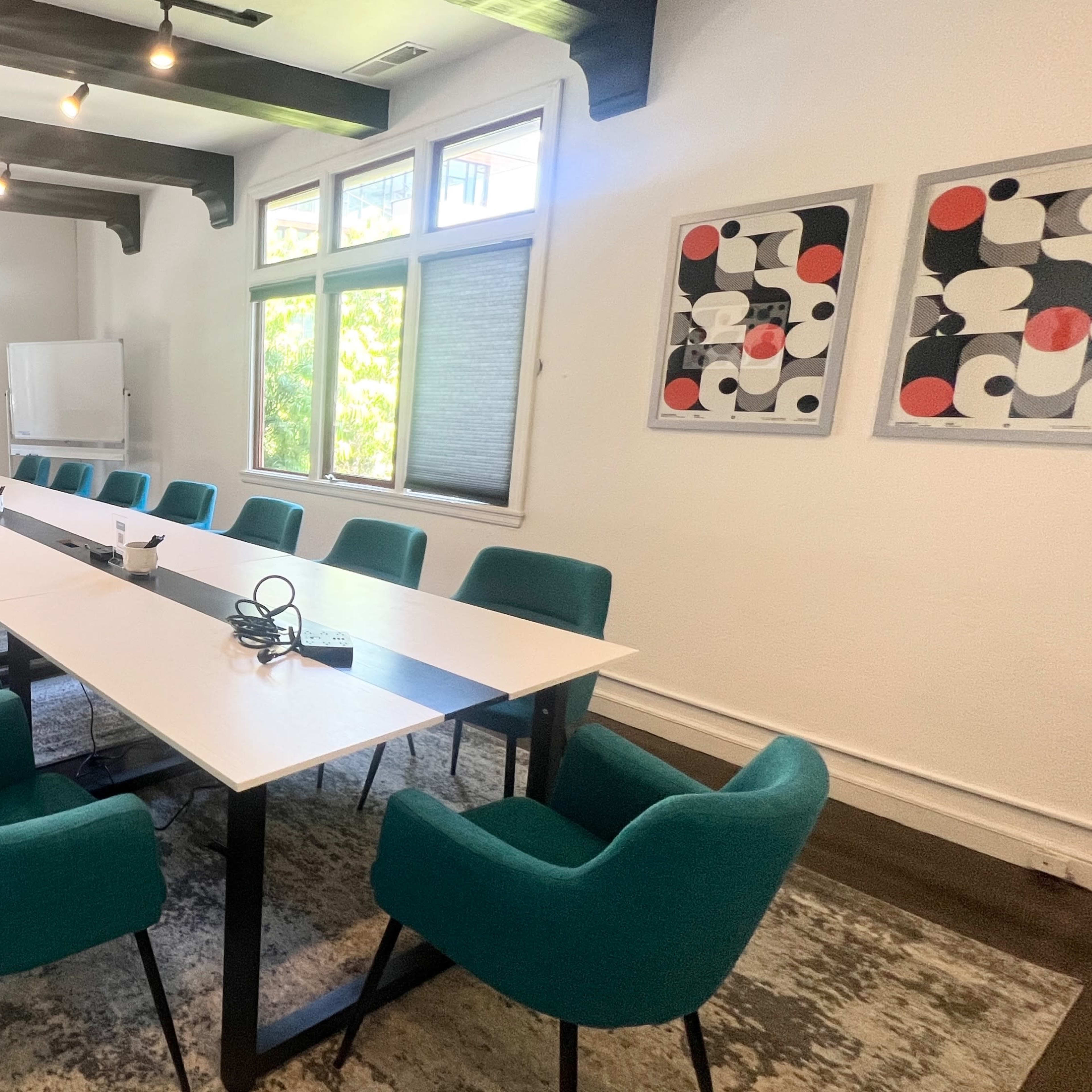 A long conference table with teal chairs is set up in a room featuring a fireplace, large windows, and modern artwork on the walls.