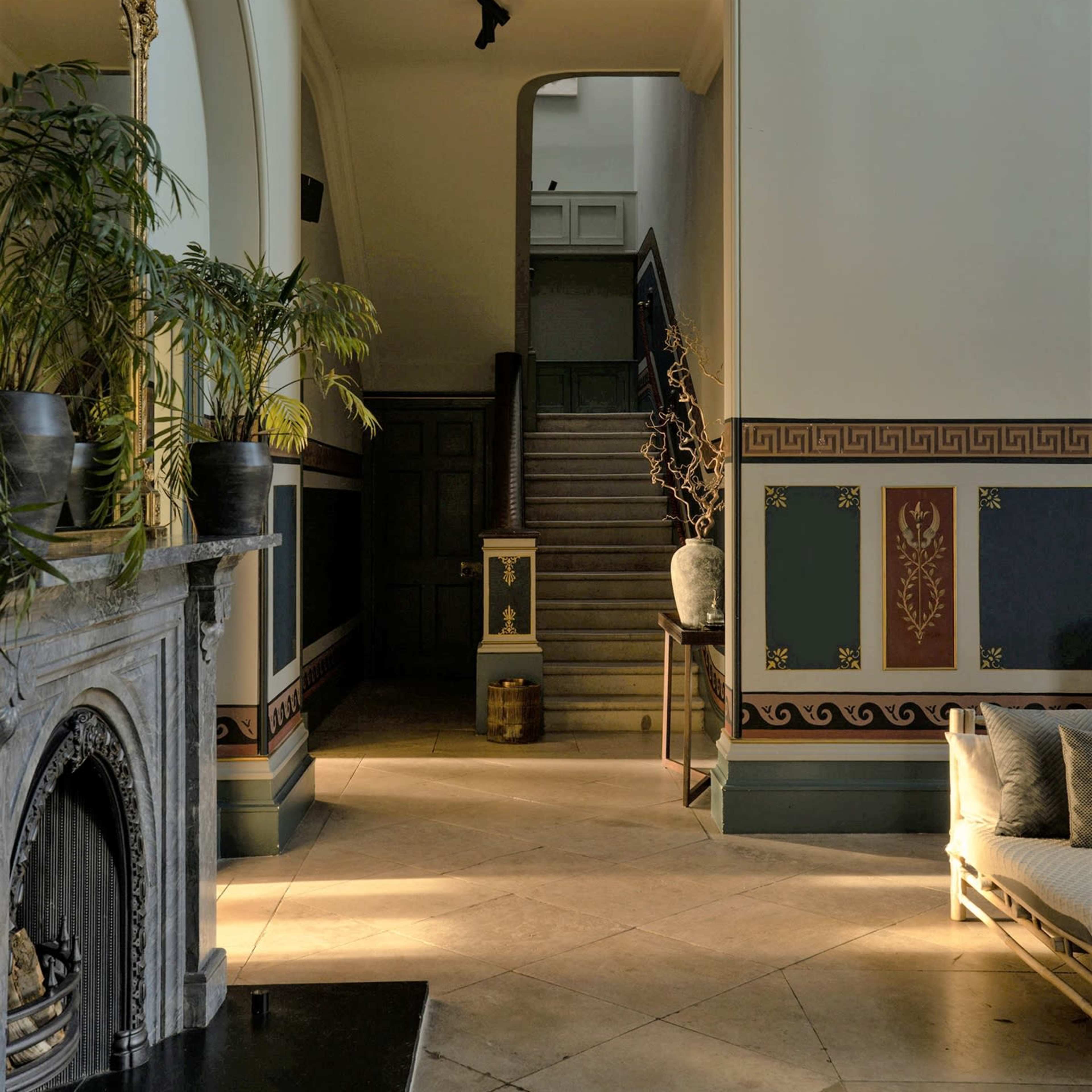 A spacious hallway with a staircase, decorated walls, a fireplace, and plants positioned near a seating area.