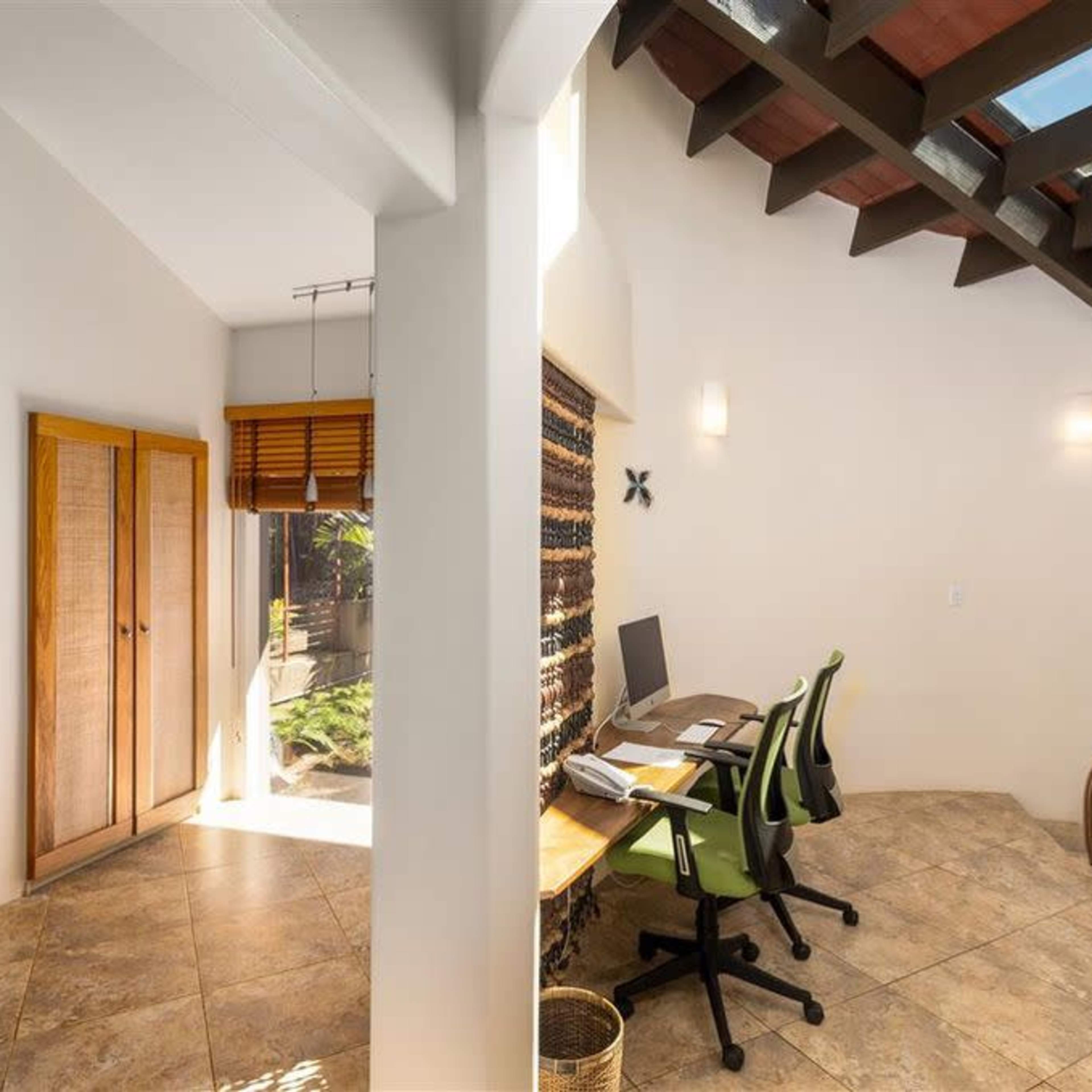 A bright interior space featuring a hallway with wooden sliding doors on one side and a small office area with a desk and chairs on the other.