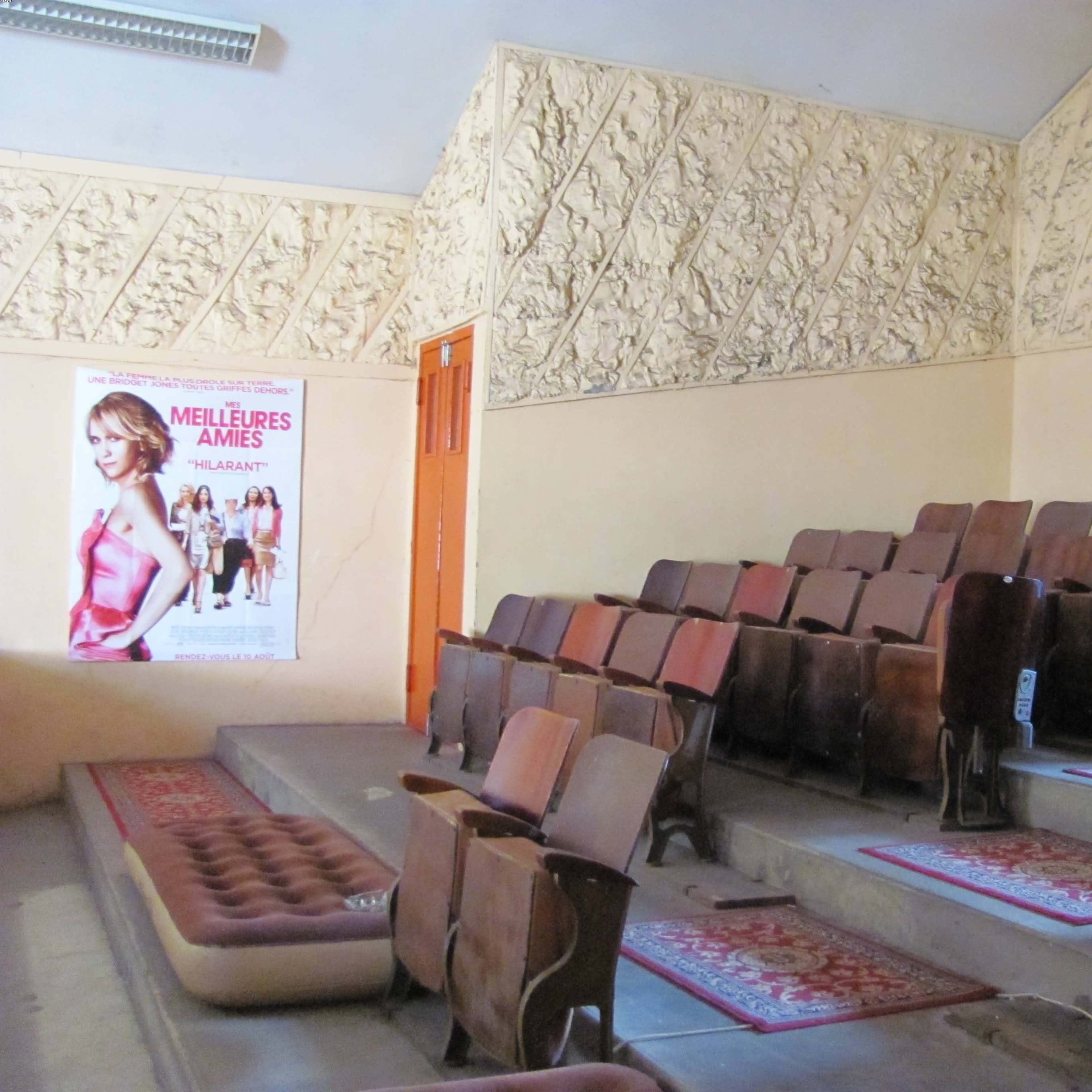 A small, empty cinema with rows of wooden seats and a decorative textured wall, along with a movie poster on one side.
