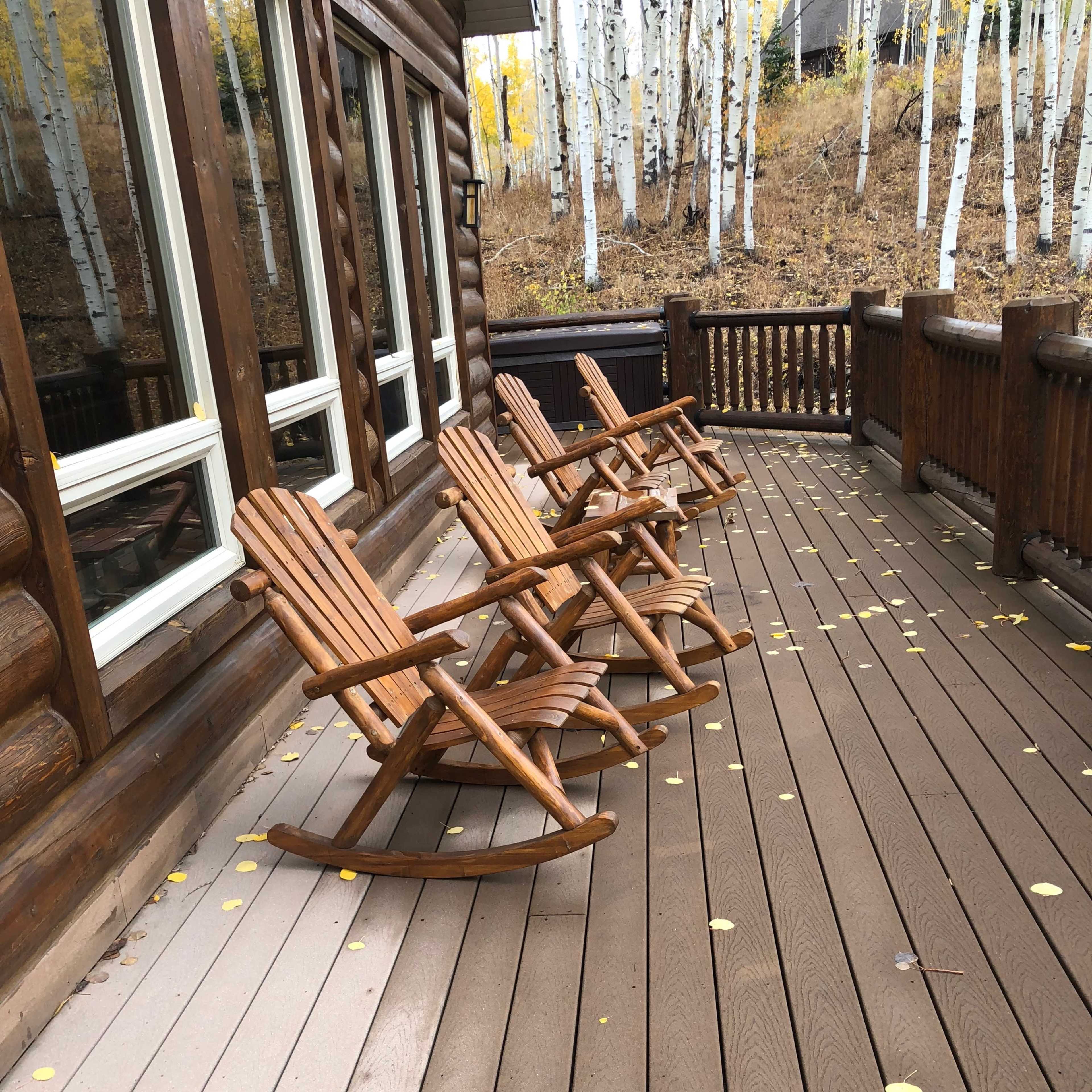 Four wooden rocking chairs are arranged on a deck made of brown planks, surrounded by aspen trees with yellow leaves in the background.