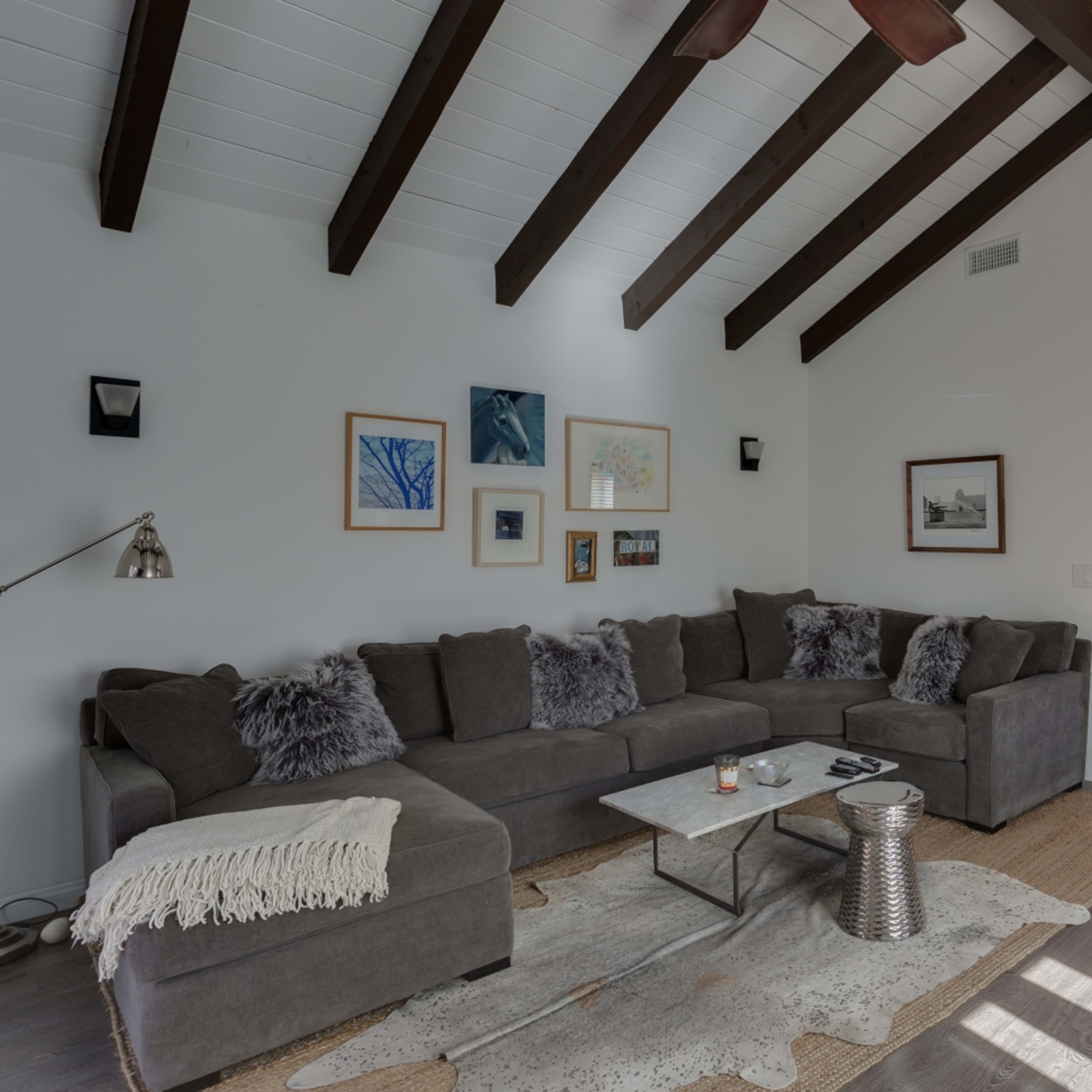 A modern living room features a sectional sofa, decorative art on the walls, and a view into a kitchen with wooden cabinets.