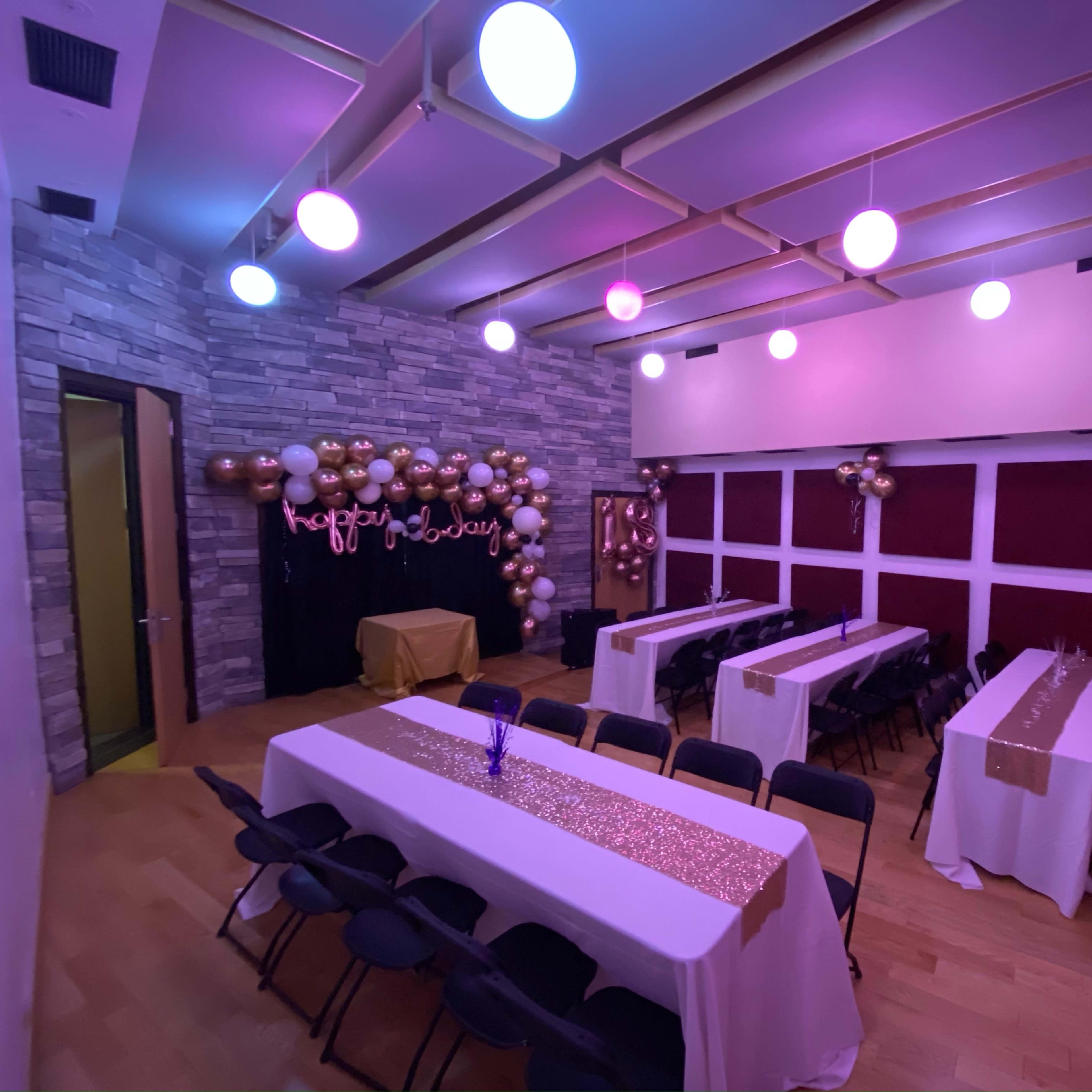 An event space with tables covered in white and gold decor, balloons, and decorative lighting.