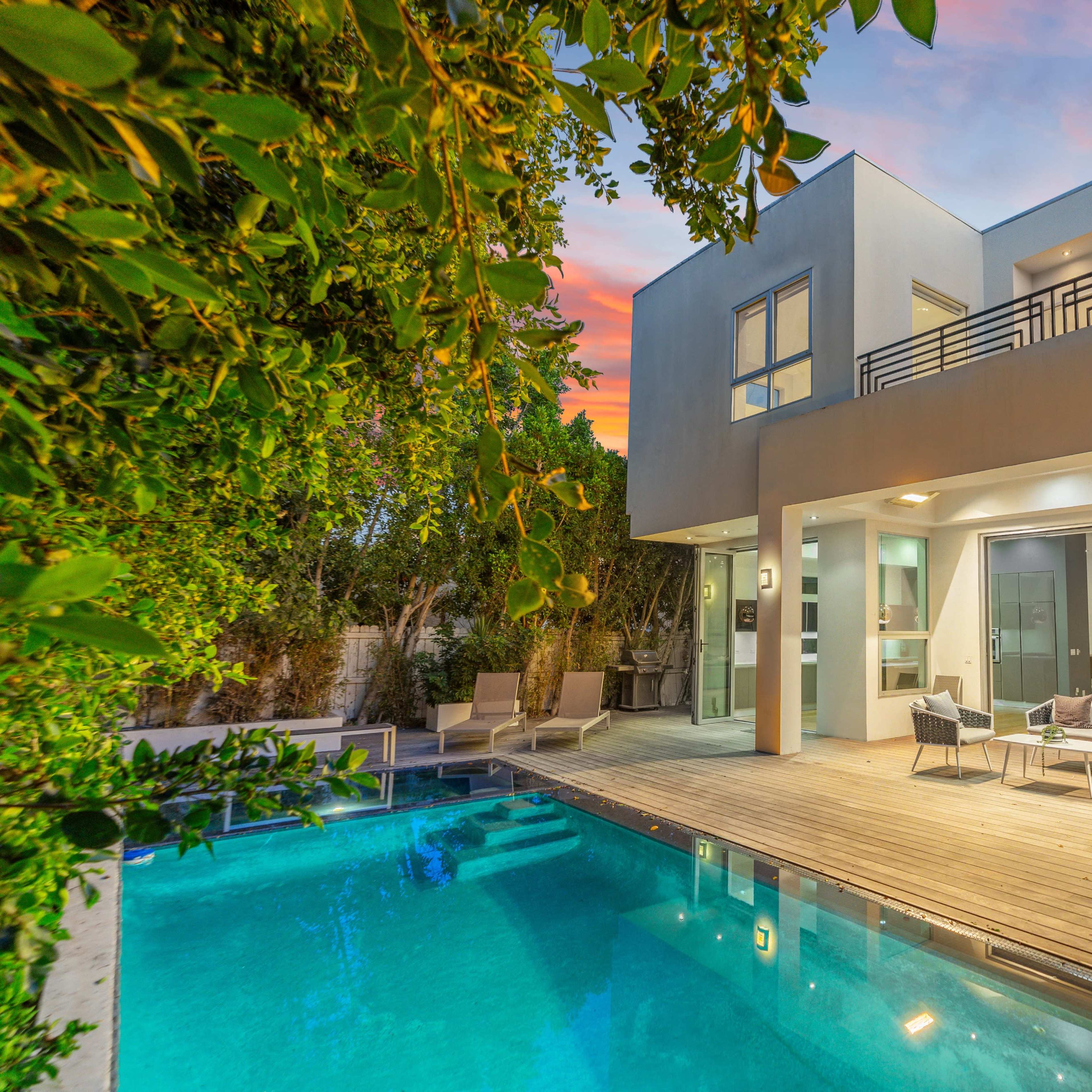 A modern house with a swimming pool and outdoor seating area is surrounded by lush greenery.