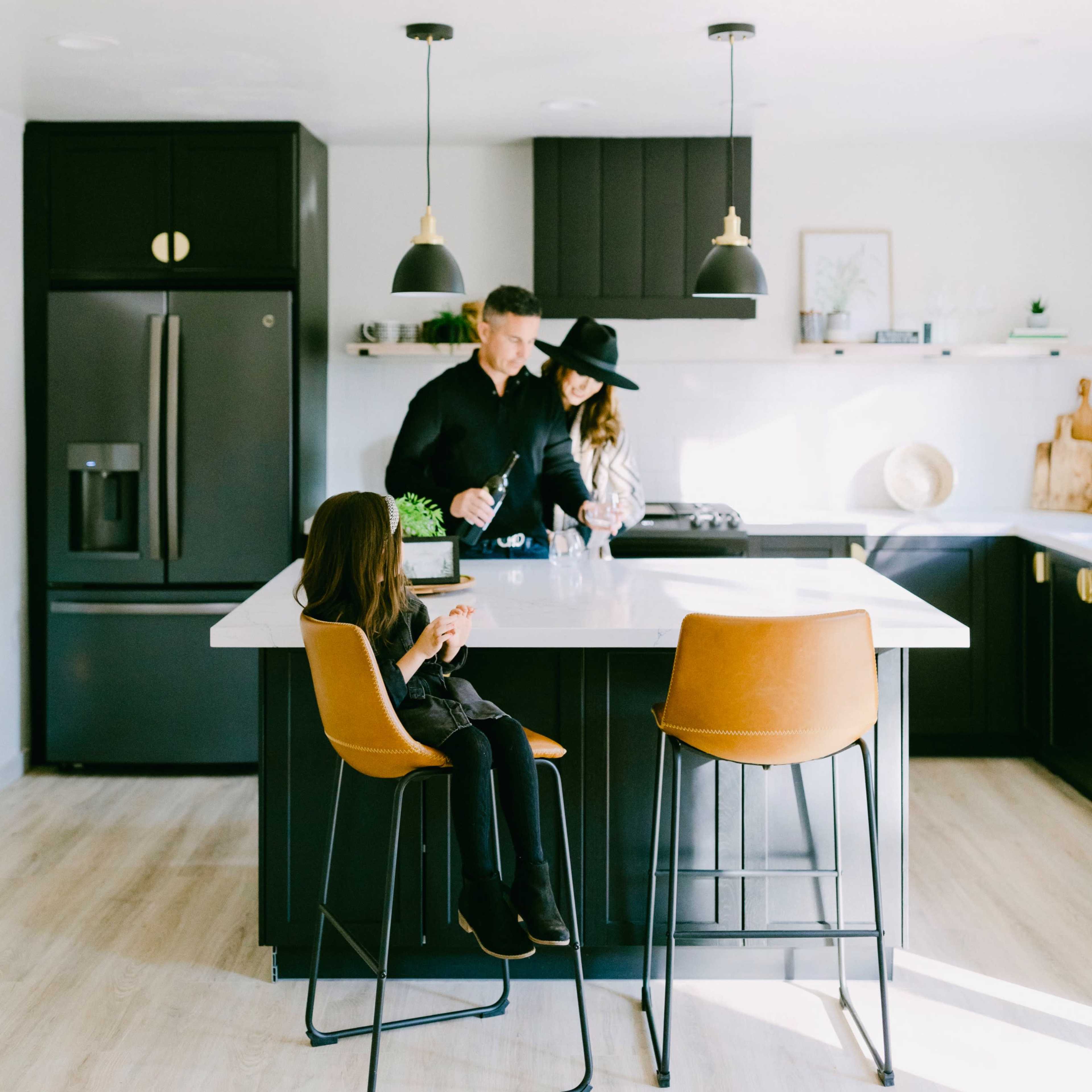 A family prepares food together in a modern kitchen with dark cabinetry and a light countertop.