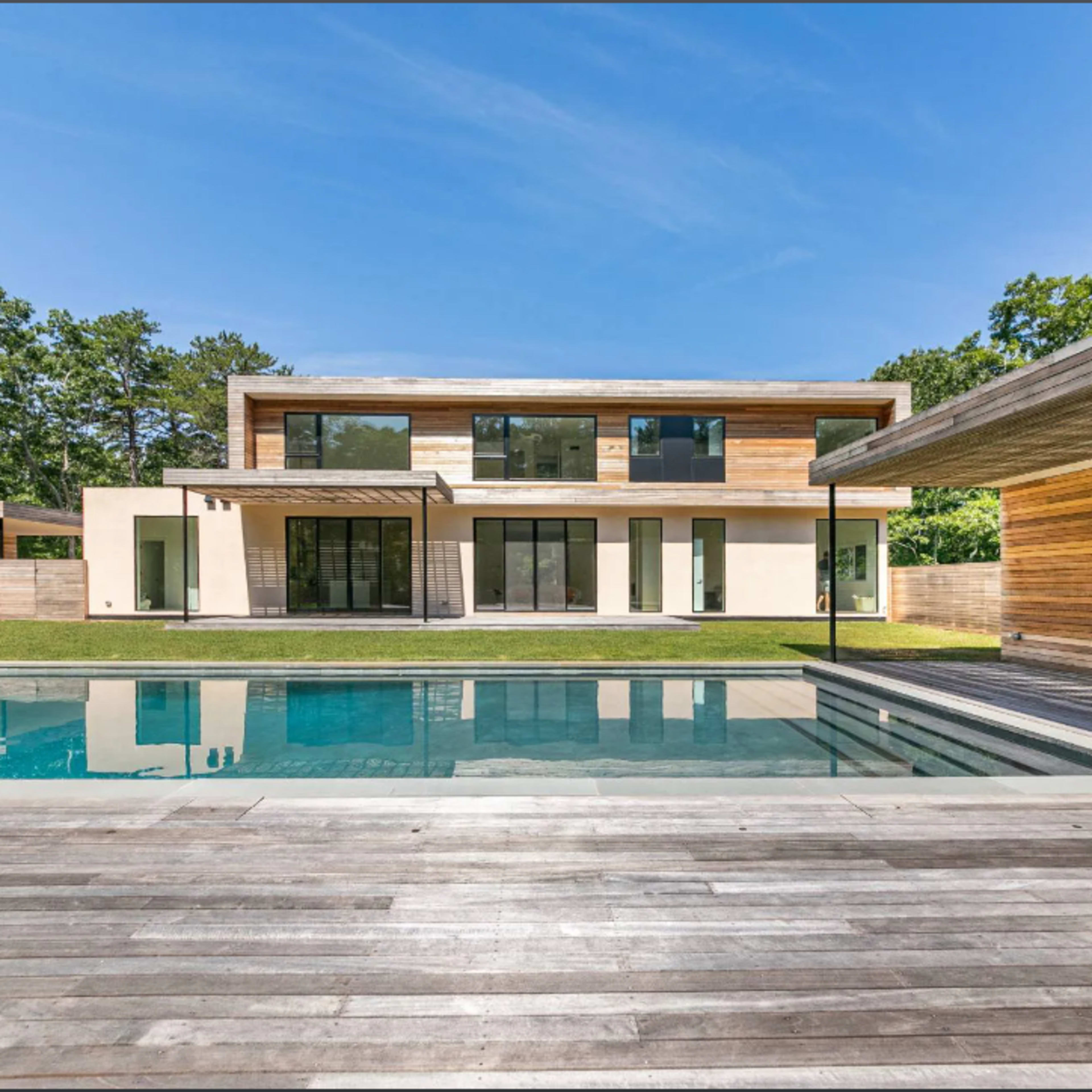 A modern two-story house with a pool is surrounded by greenery and features large glass windows and wooden accents.