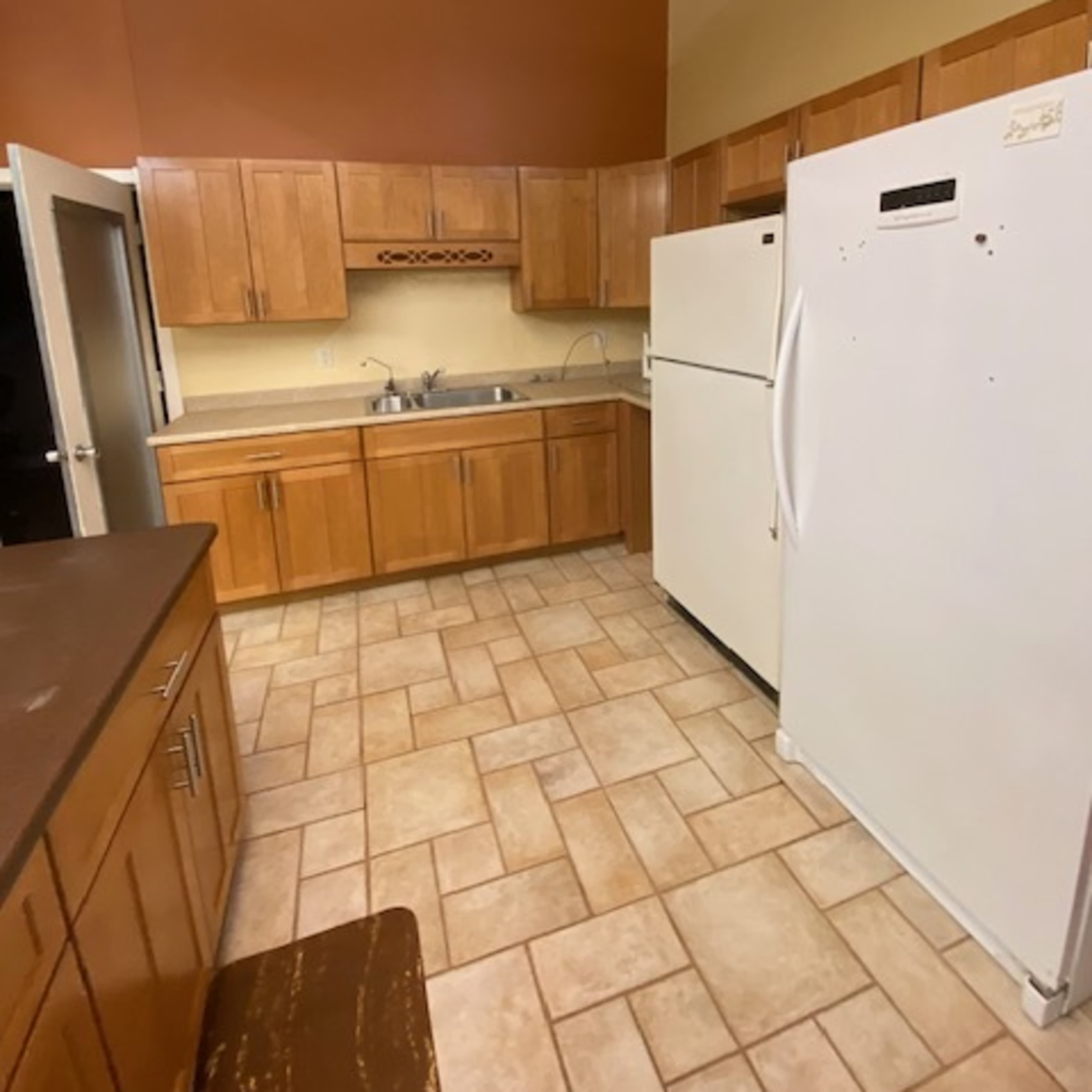 A kitchen with wooden cabinets, a white refrigerator, and tiled flooring.