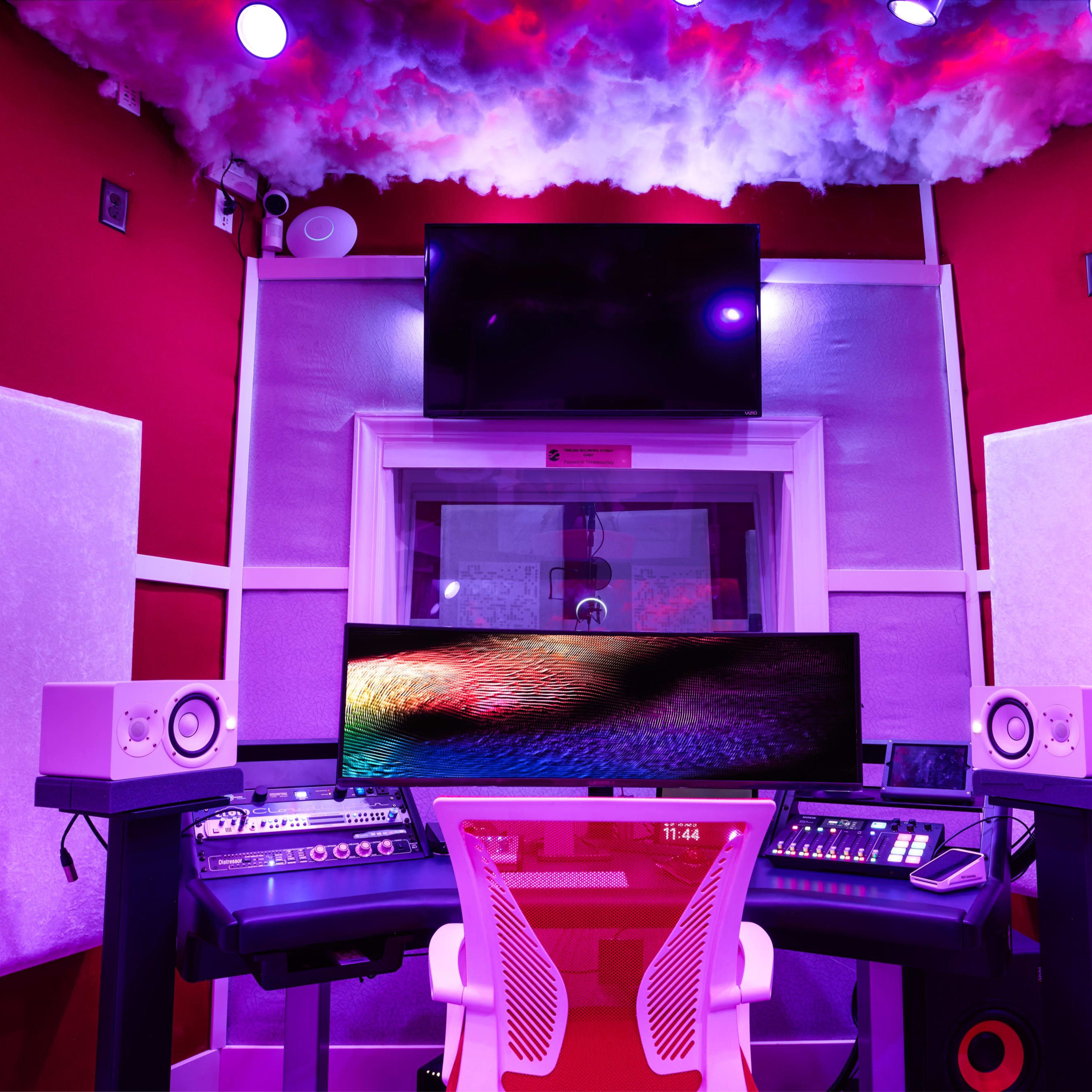 A modern recording studio with a large curved monitor, audio equipment, and soundproof panels on the walls, illuminated by purple lighting.