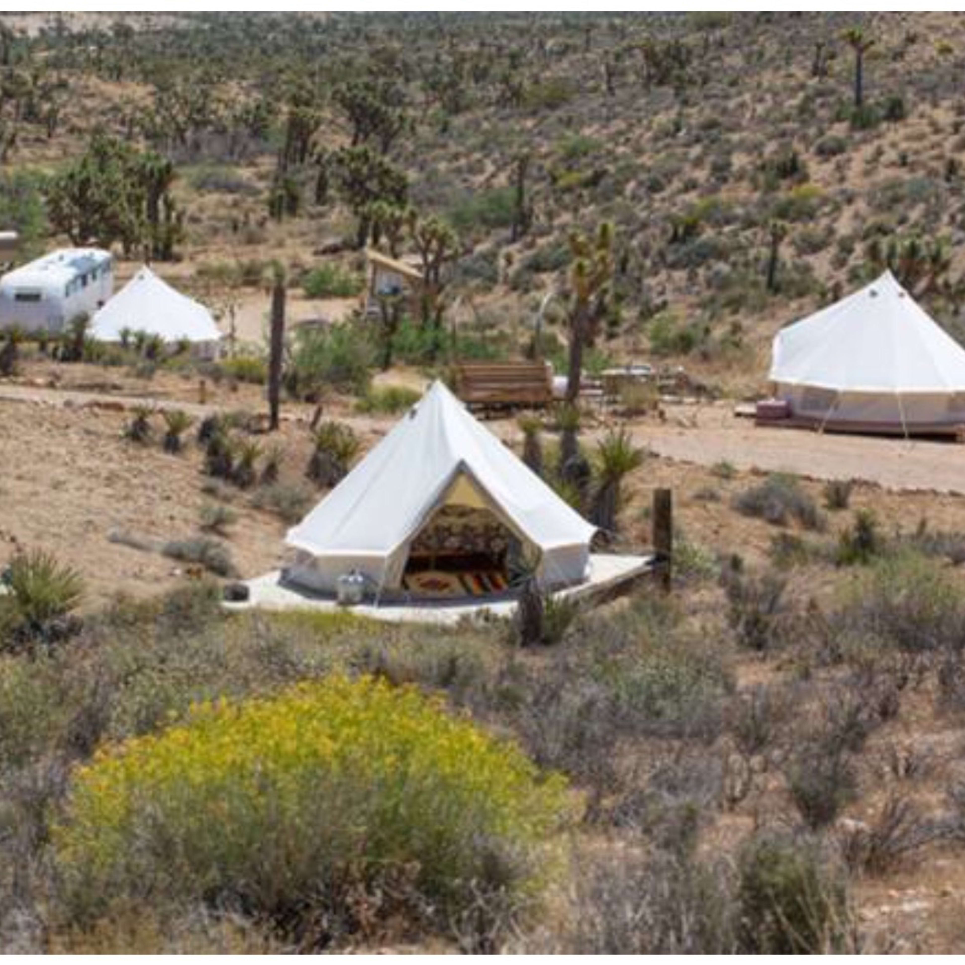 Several white tents and a trailer set up in a desert landscape with sparse vegetation and rolling hills in the background.