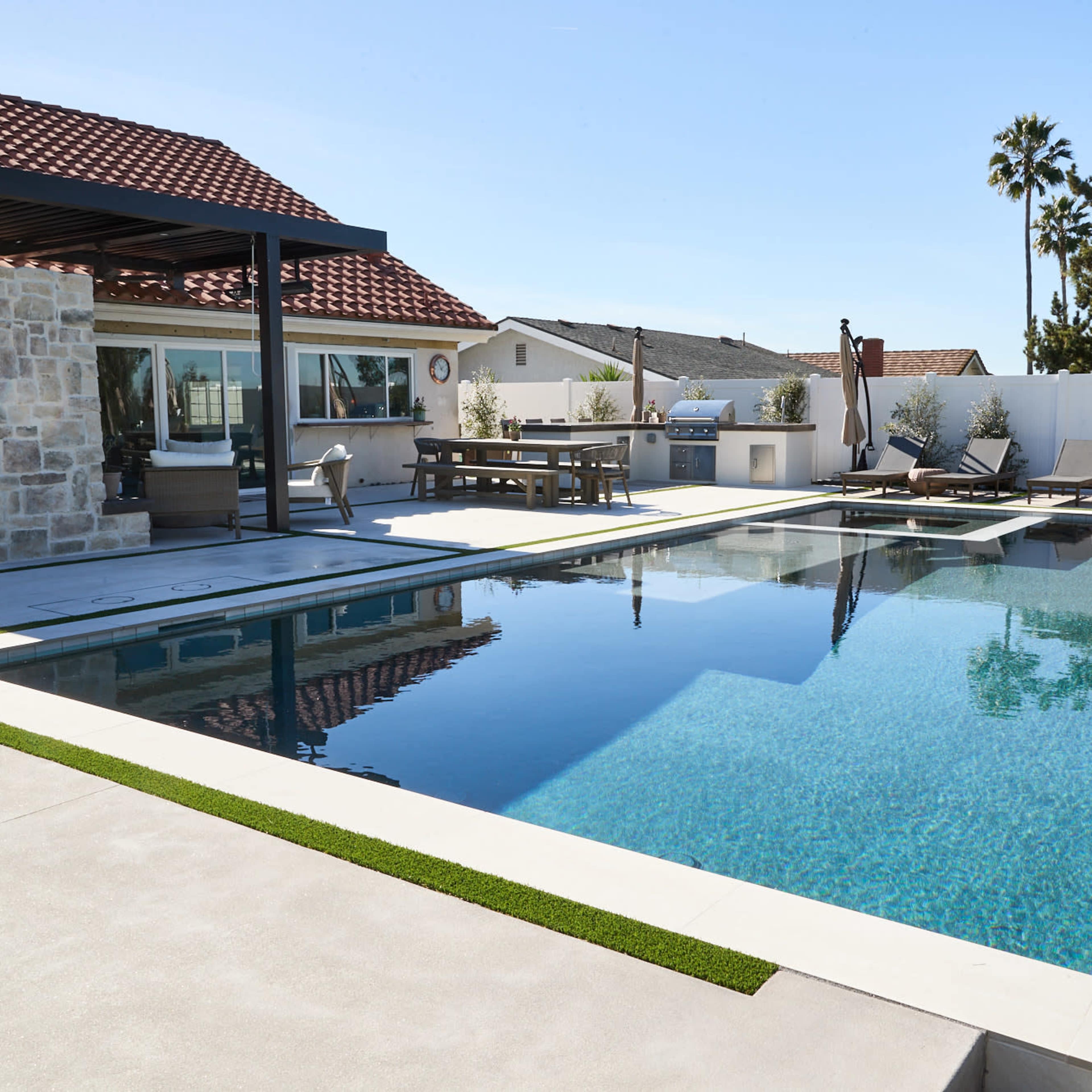 A modern outdoor pool area with a stone fireplace, lounge chairs, and a shaded dining space under a pergola.