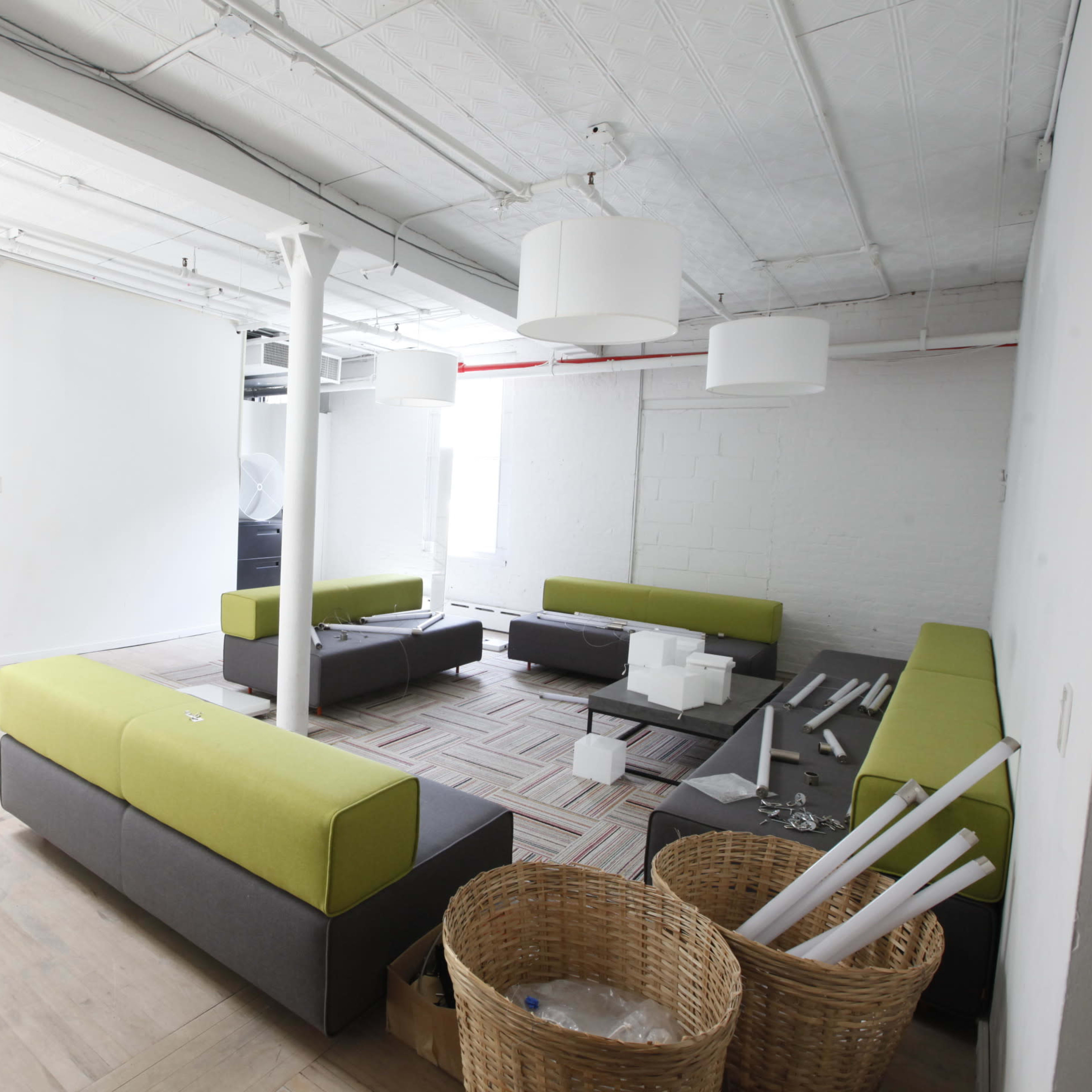 A modern office space featuring green and gray seating arrangements, a light-colored floor, and baskets containing miscellaneous items.
