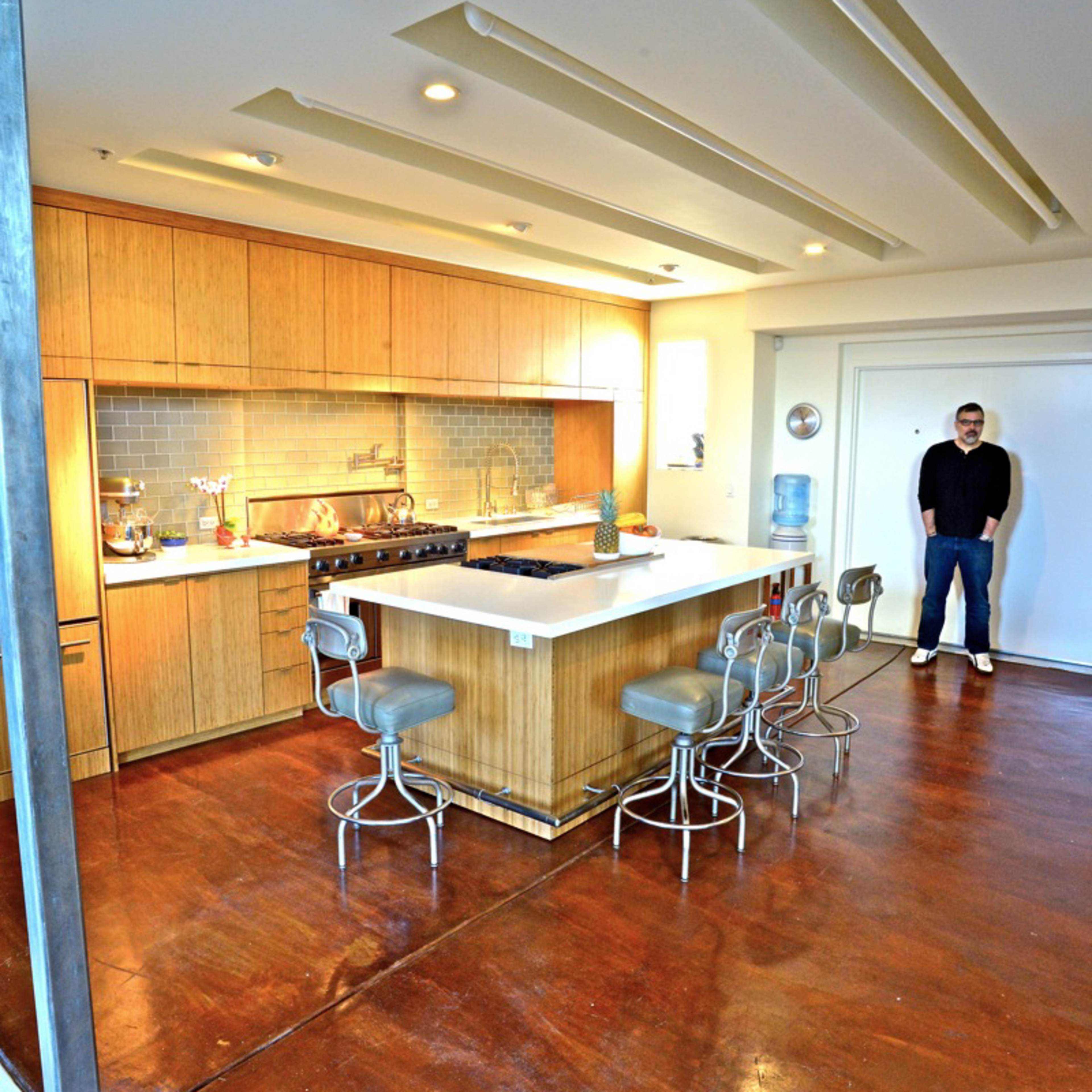 A modern kitchen features wooden cabinetry, an island with seating, and a standing person next to a water cooler.