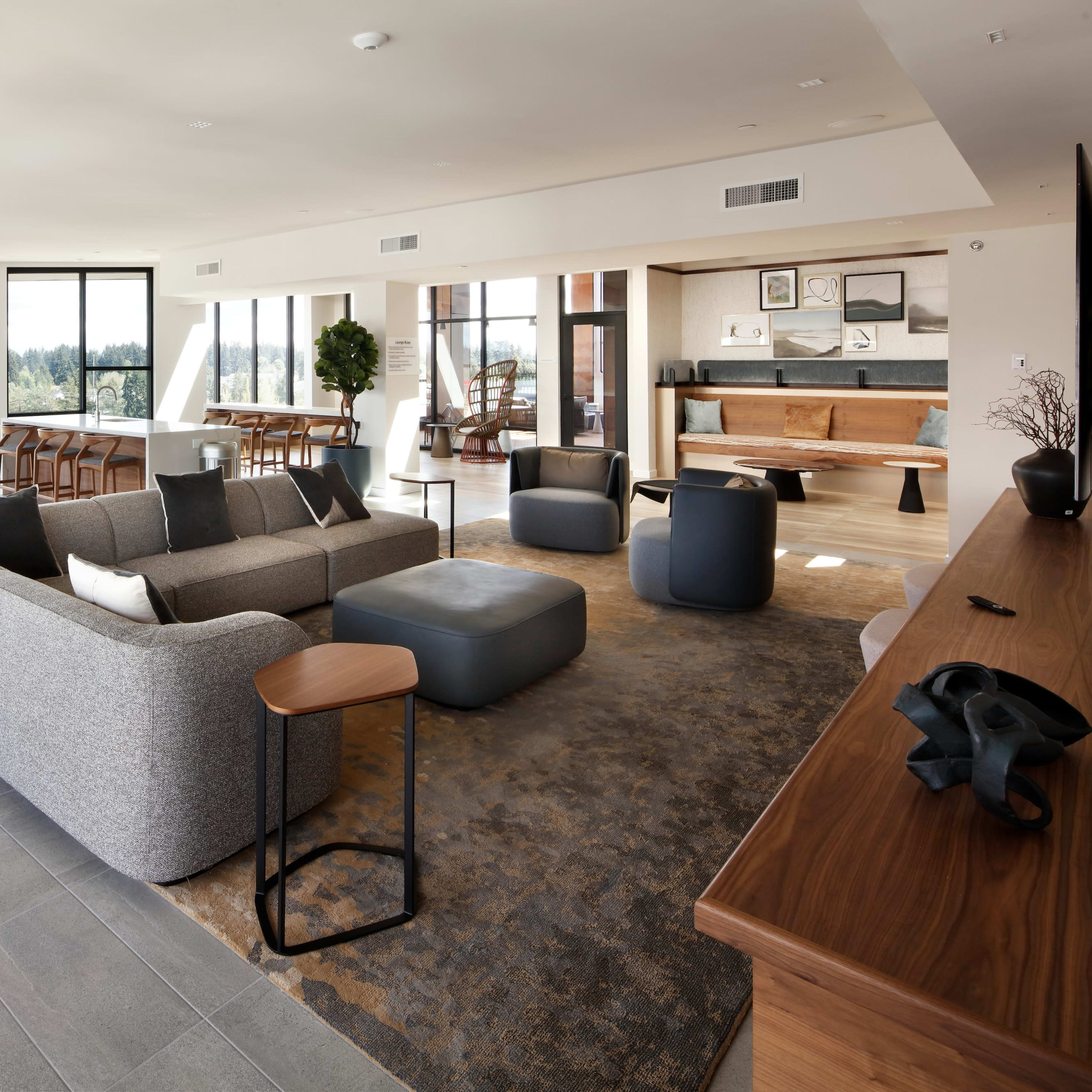 A modern open-concept living space with a gray sofa, a coffee table, and various seating arrangements, featuring large windows that provide natural light.