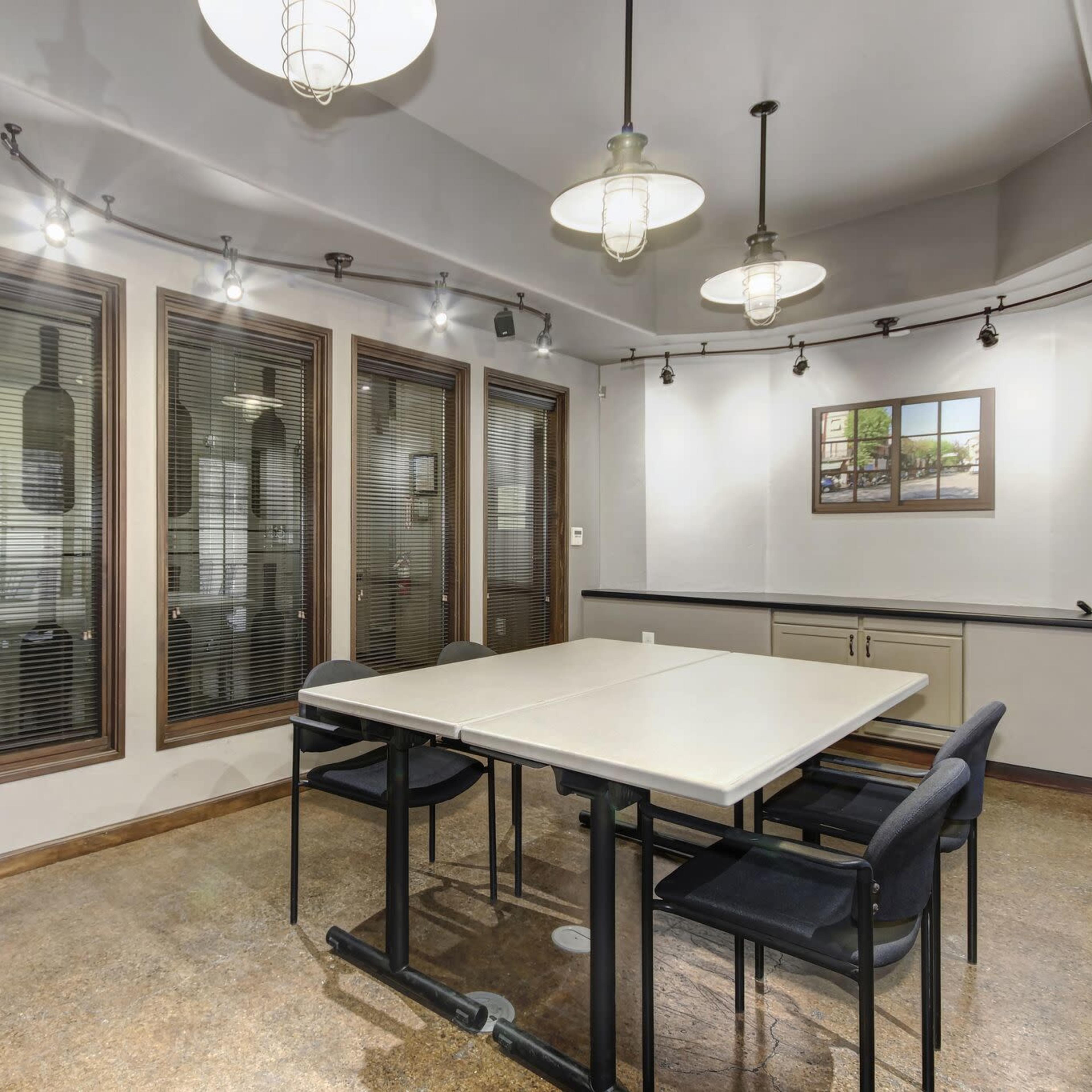 A modern meeting room with a large table surrounded by black chairs, and large windows with blinds offering a view of the outside.