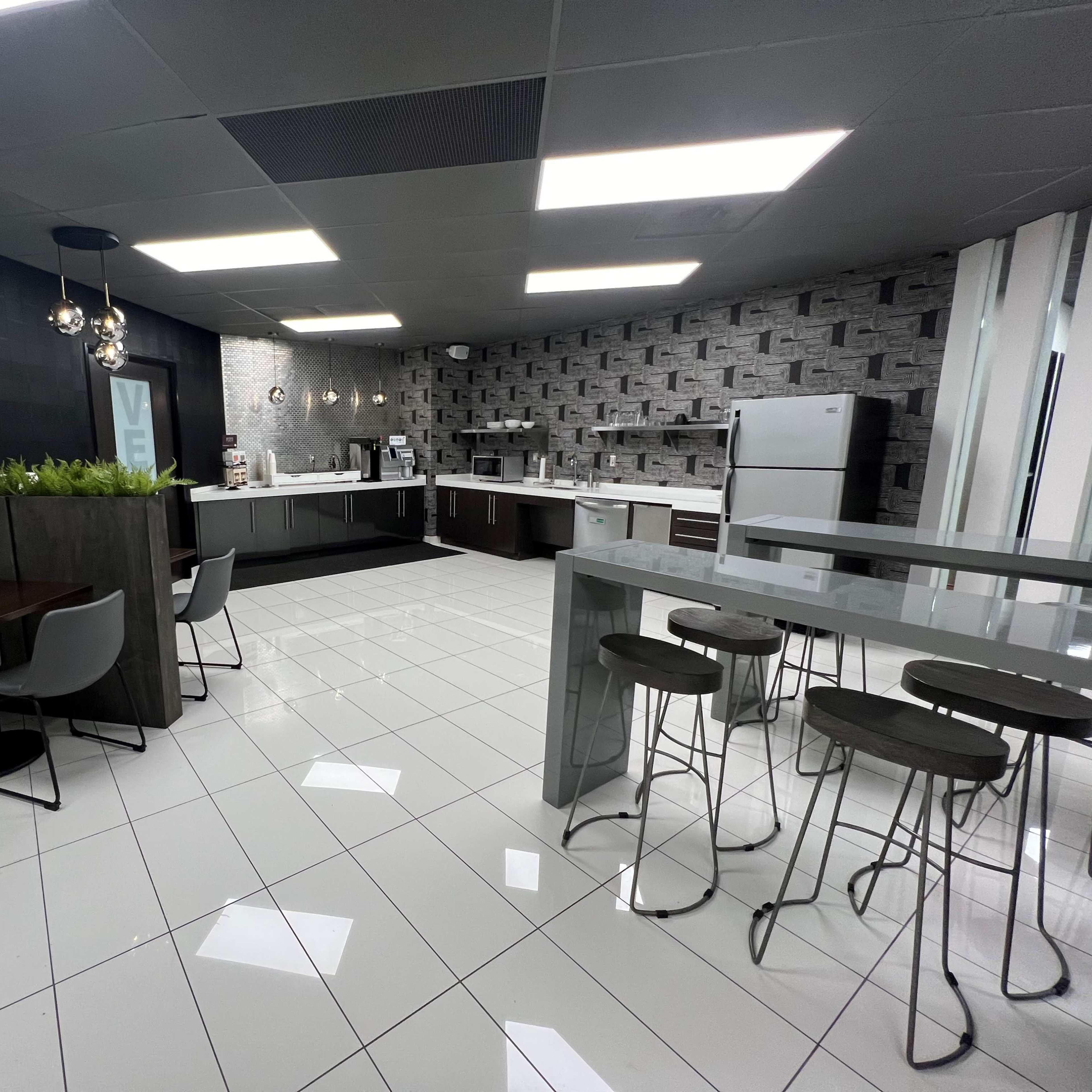 A modern kitchen space featuring sleek cabinets, a dining area with white booths, and a bar-height table with stools, all set against a tiled floor.