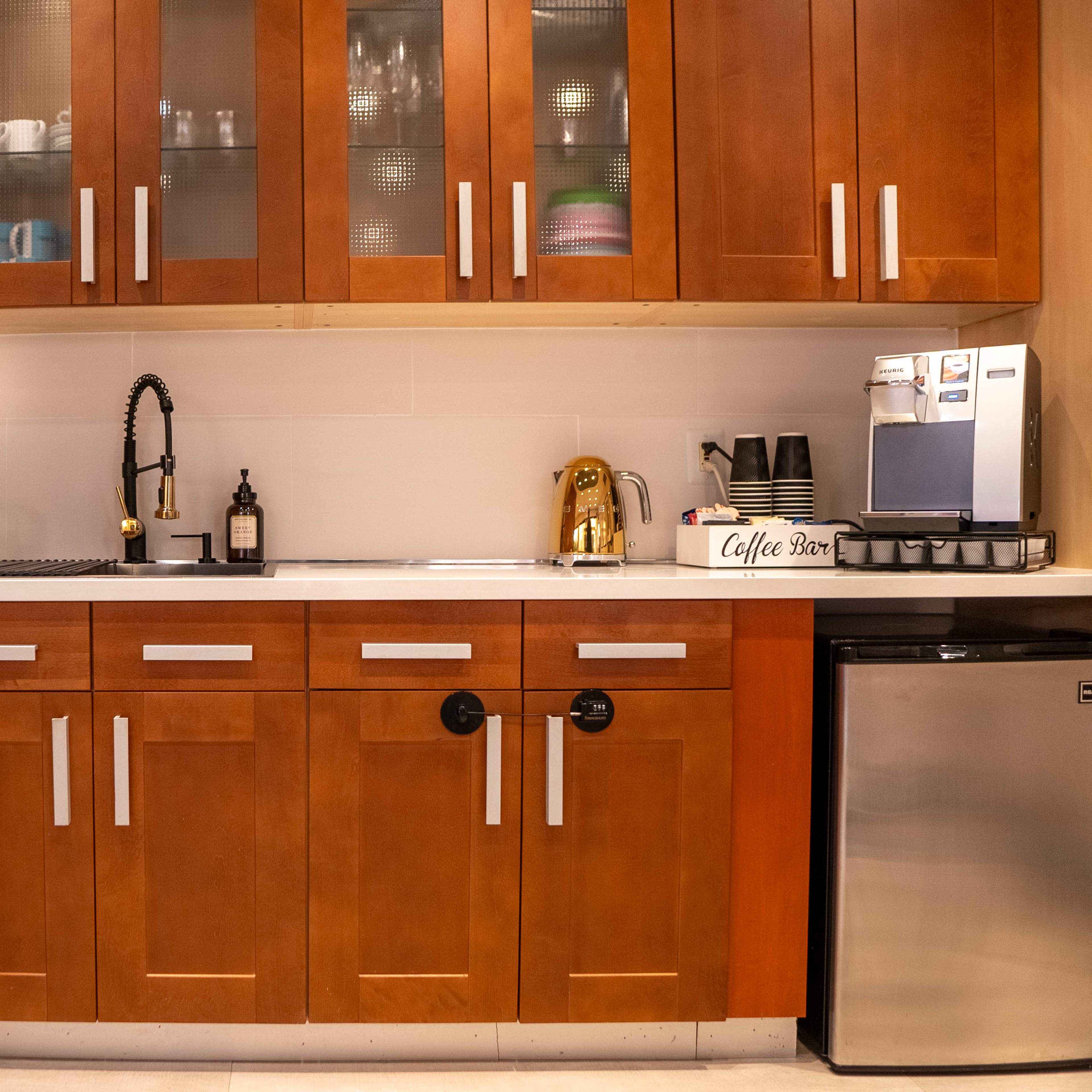 A kitchen with wooden cabinets, a sink with a black faucet, a coffee machine, and an assortment of kitchenware displayed on the countertop.