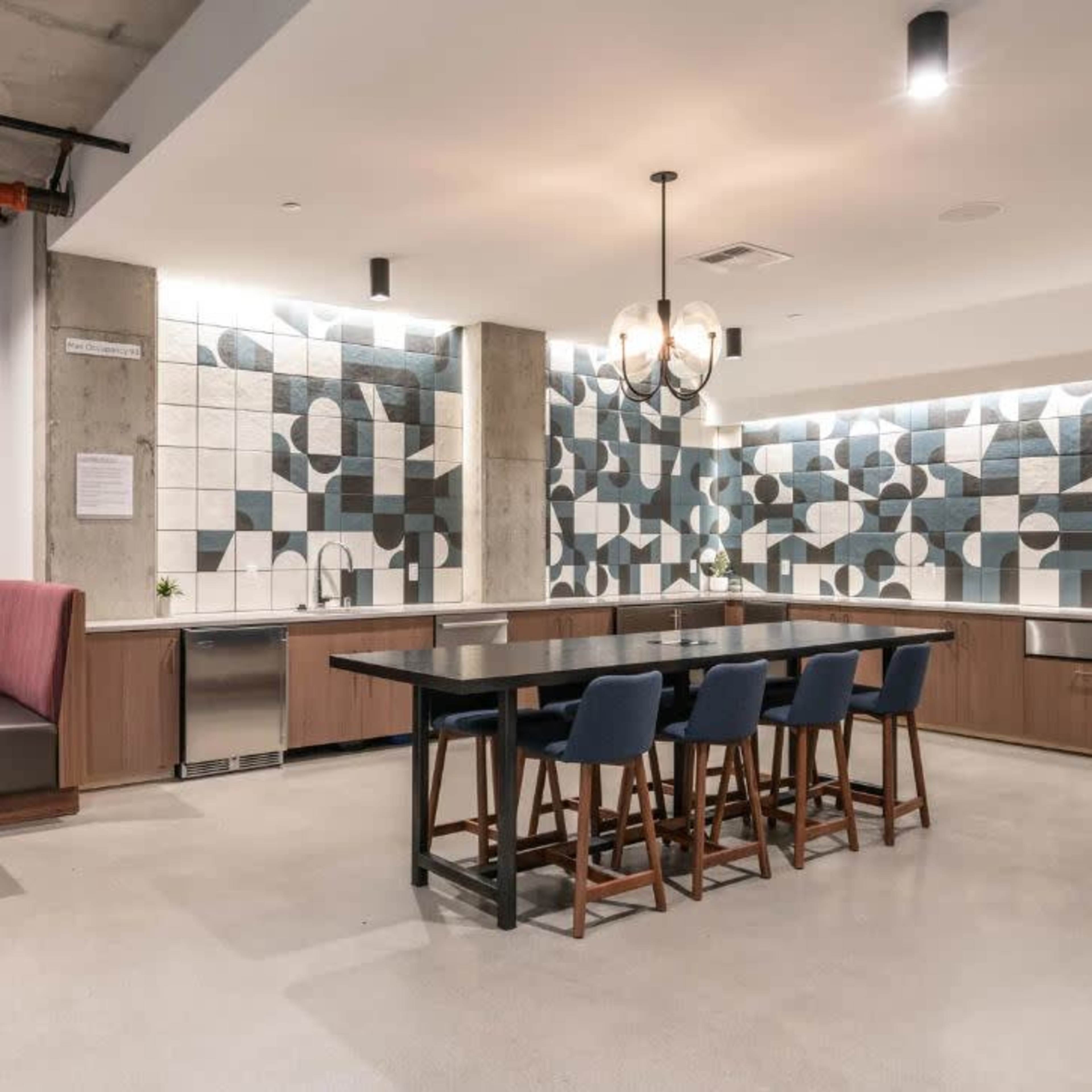 A modern kitchen featuring a geometric tiled backsplash, wooden cabinetry, a central island with bar seating, and a cozy booth seating area.