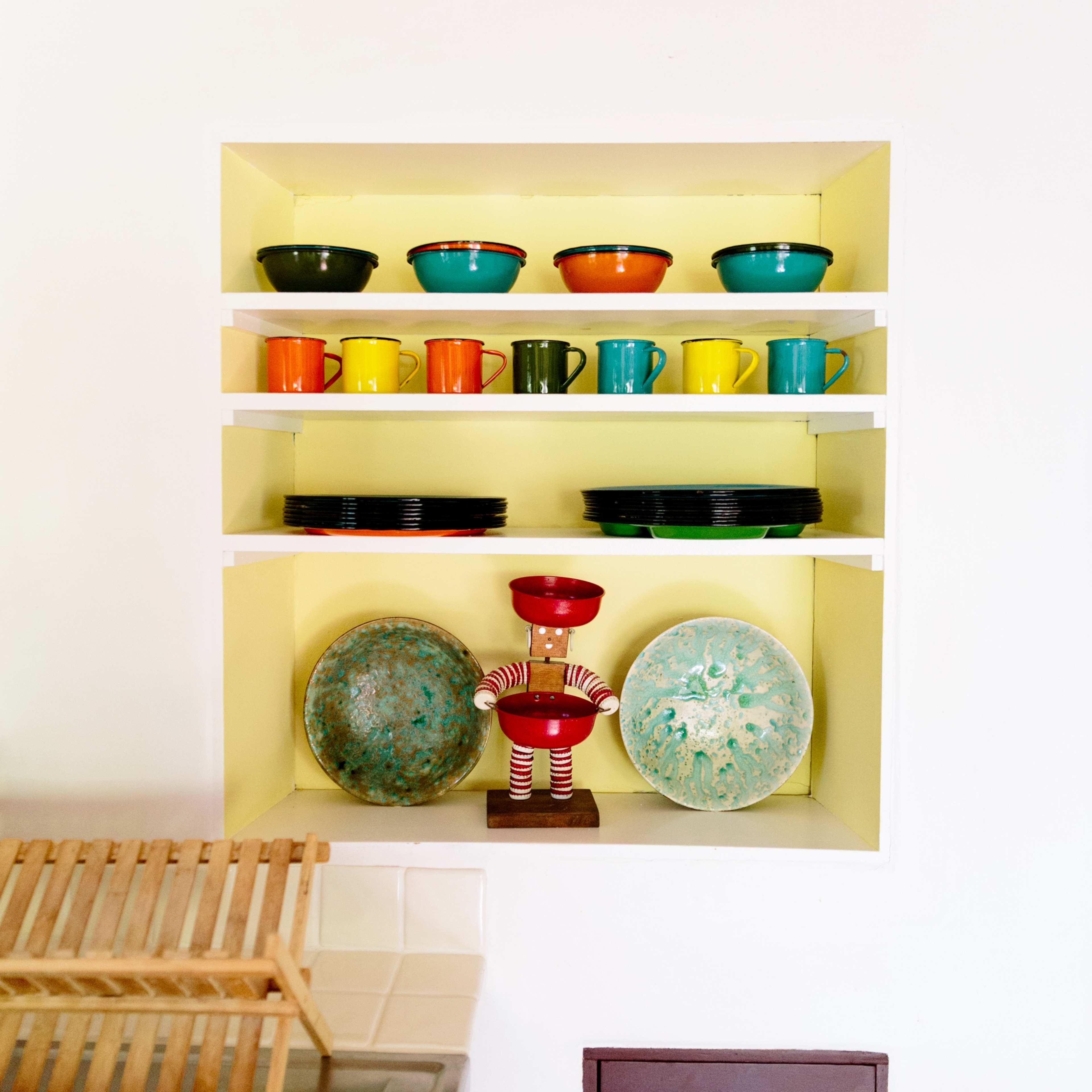 A wall-mounted shelf displays a variety of colorful bowls, cups, and dishes, along with a decorative figure in the center.