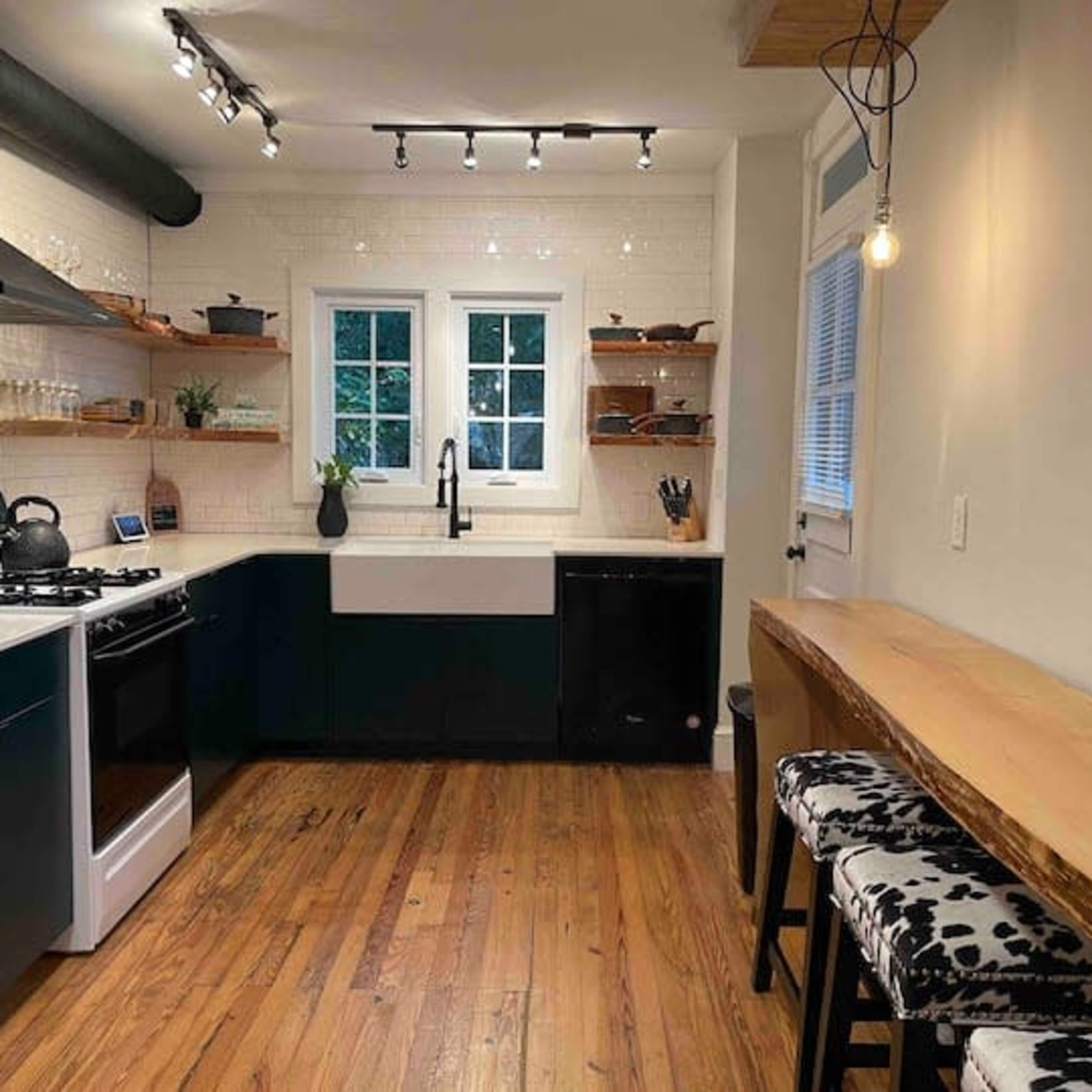 A modern kitchen featuring a black and white color scheme, with wooden shelves, a farmhouse sink, and a small dining area with bar stools.