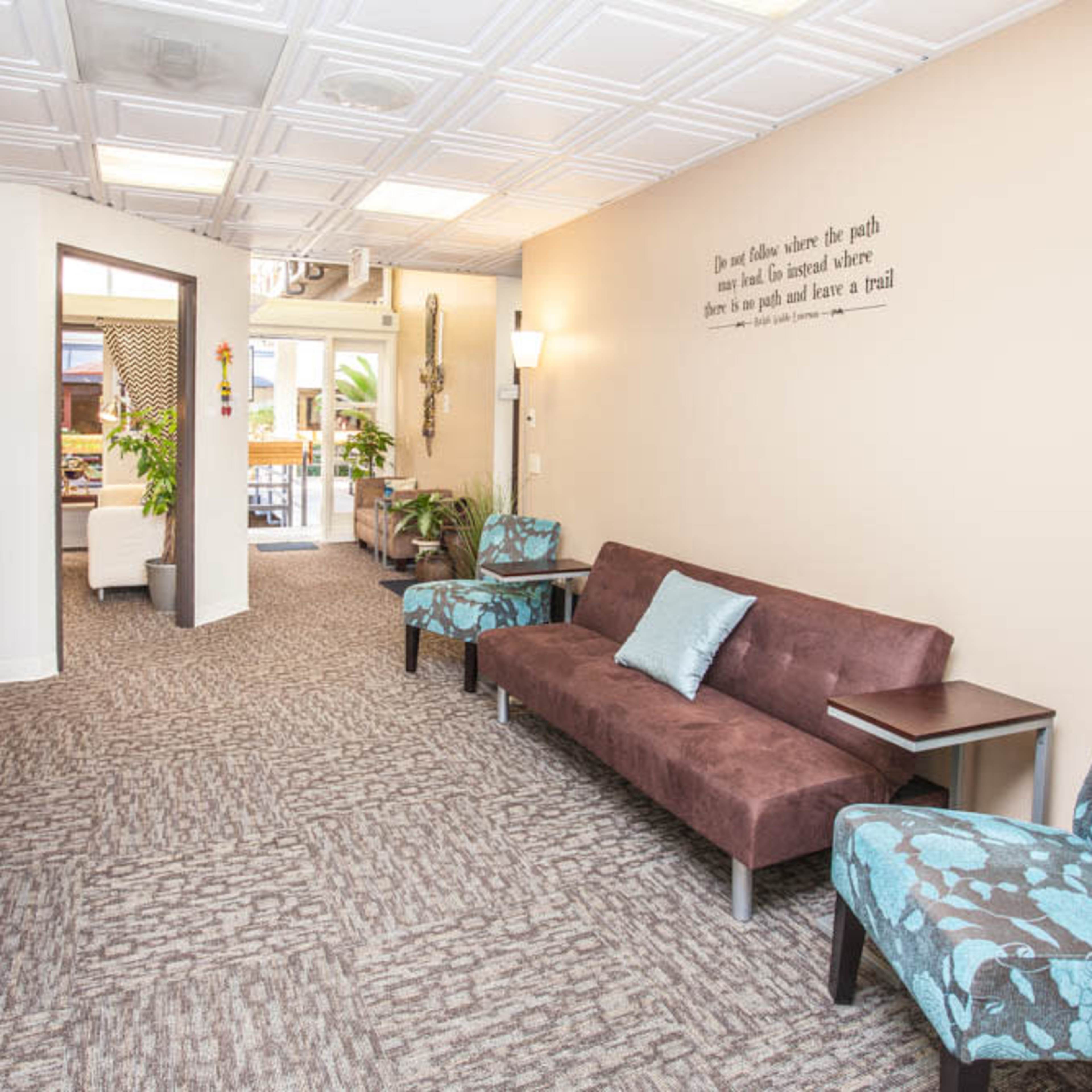 A modern office corridor with a seating area, a bookshelf, and decorative plants.