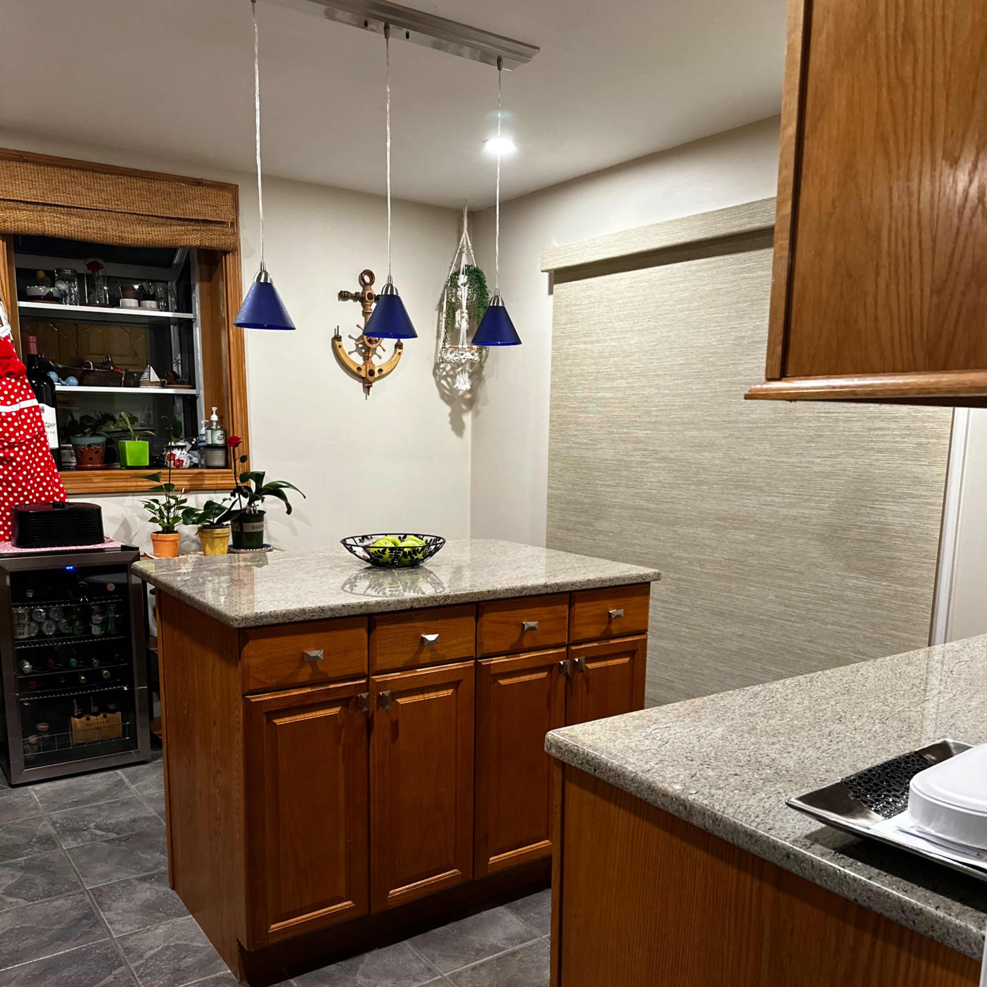A modern kitchen with wooden cabinetry, a central island with a granite countertop, and pendant lights hanging above.