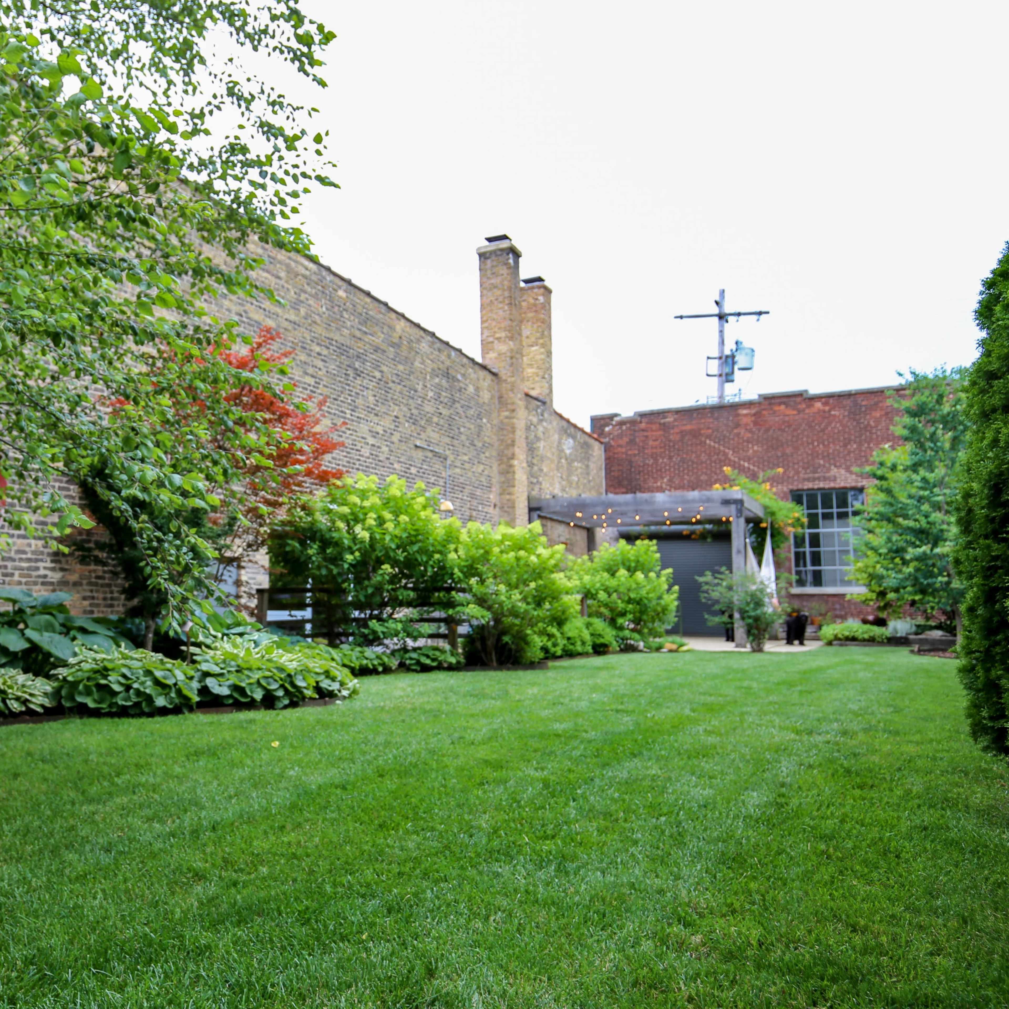 A well-maintained garden area with lush greenery, bordered by a brick wall and featuring a few small trees and plants.