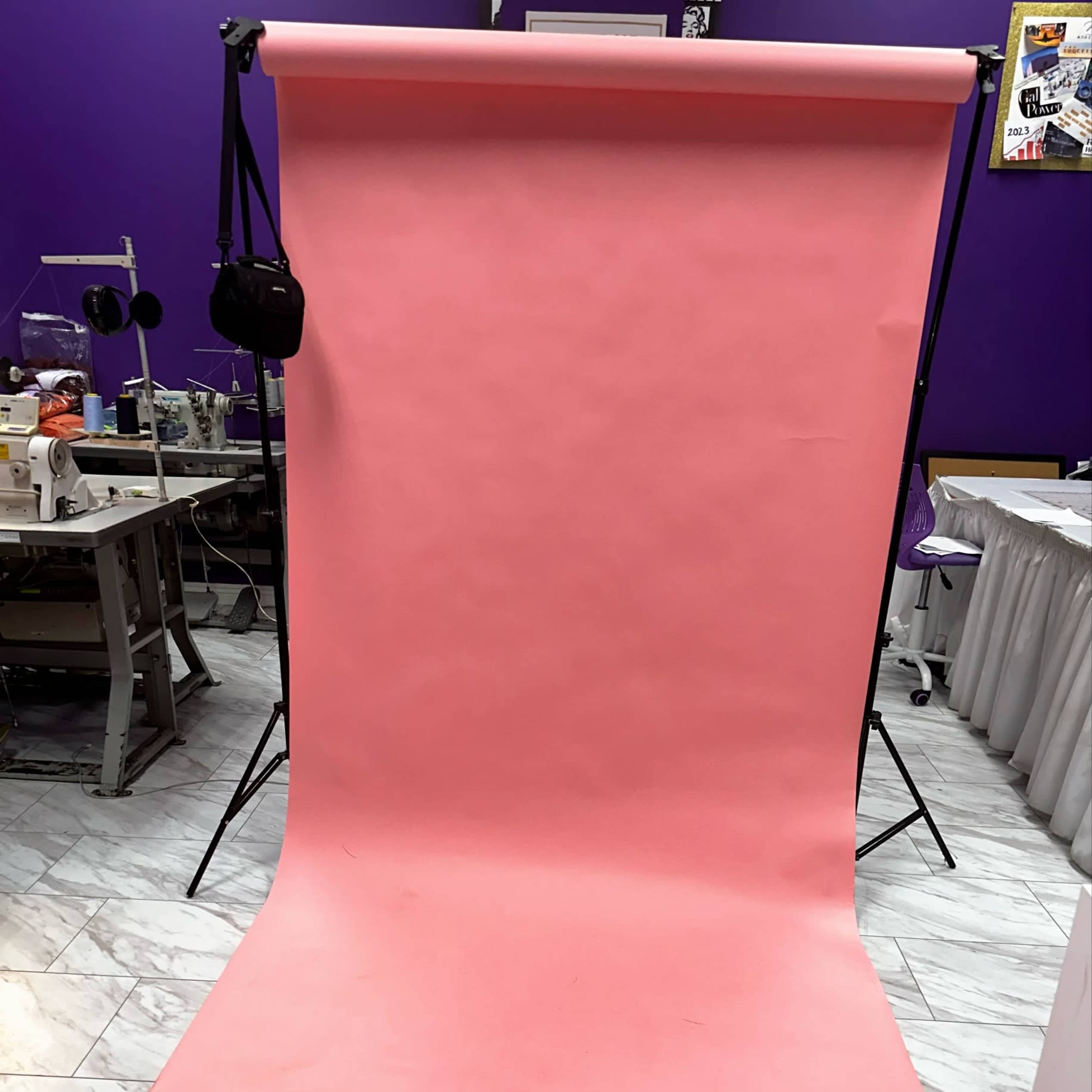A pink backdrop set up on a stand with a wooden floor beneath it in a studio environment.